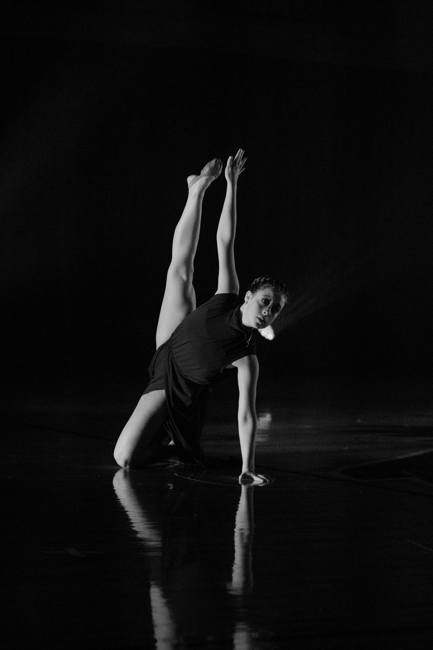 Dancer in dark attire performs emotive floor choreography against black background in dramatic monochrome.