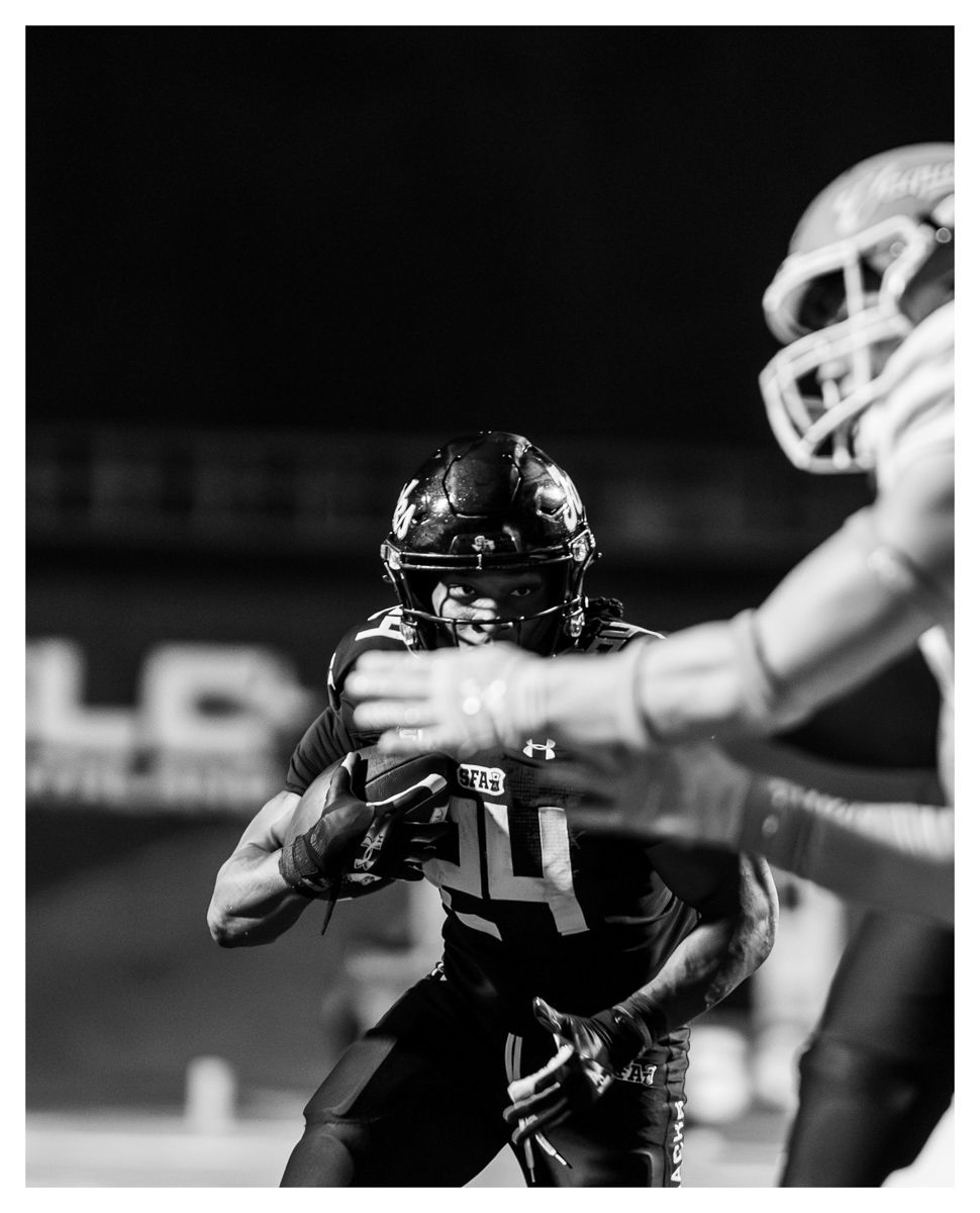 Black and white photo of a football player wearing jersey number 14 catching a pass during a night game.