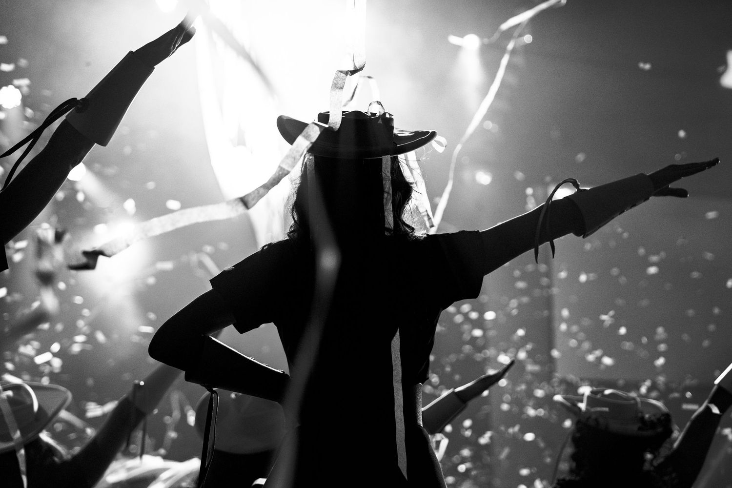 Black and white photo of a performer on stage with arms outstretched, crowd and bright lights in background.
