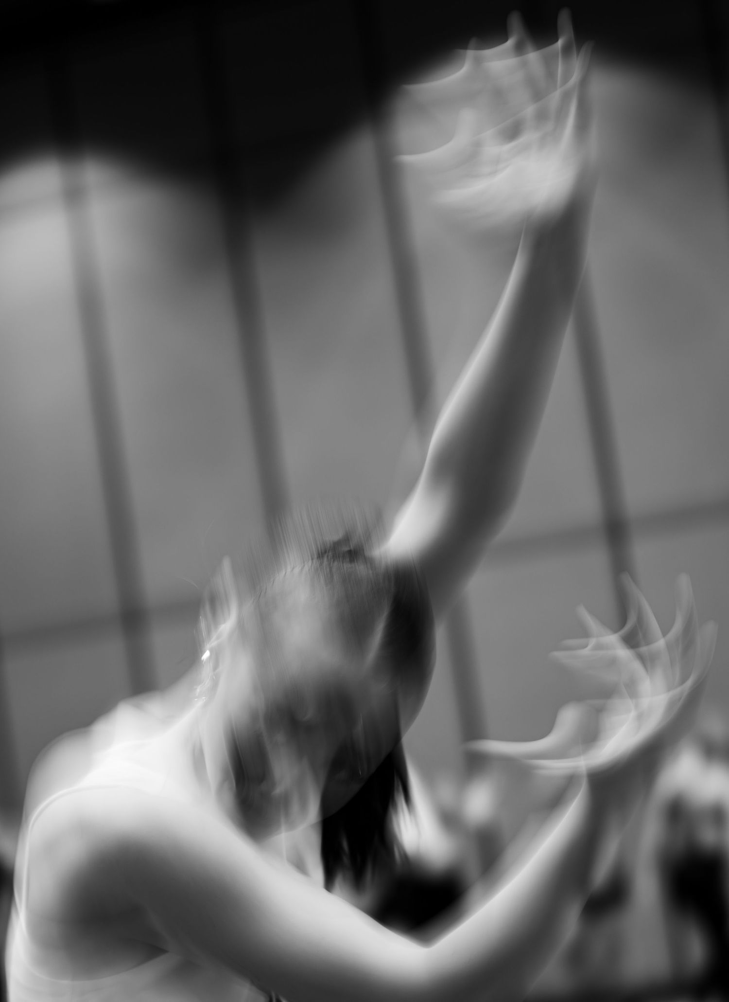 Blurred black and white photo of a dancer with arms raised gracefully in motion.