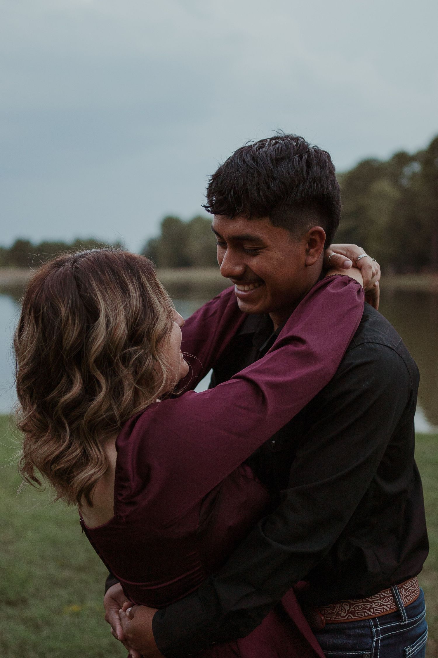 Couple embracing outdoors near lake during sunset.