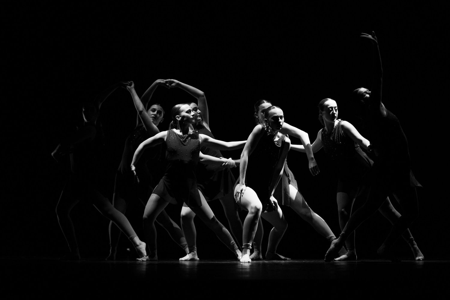 Black and white photo of contemporary dancers performing on a dark stage in expressive, dynamic poses.