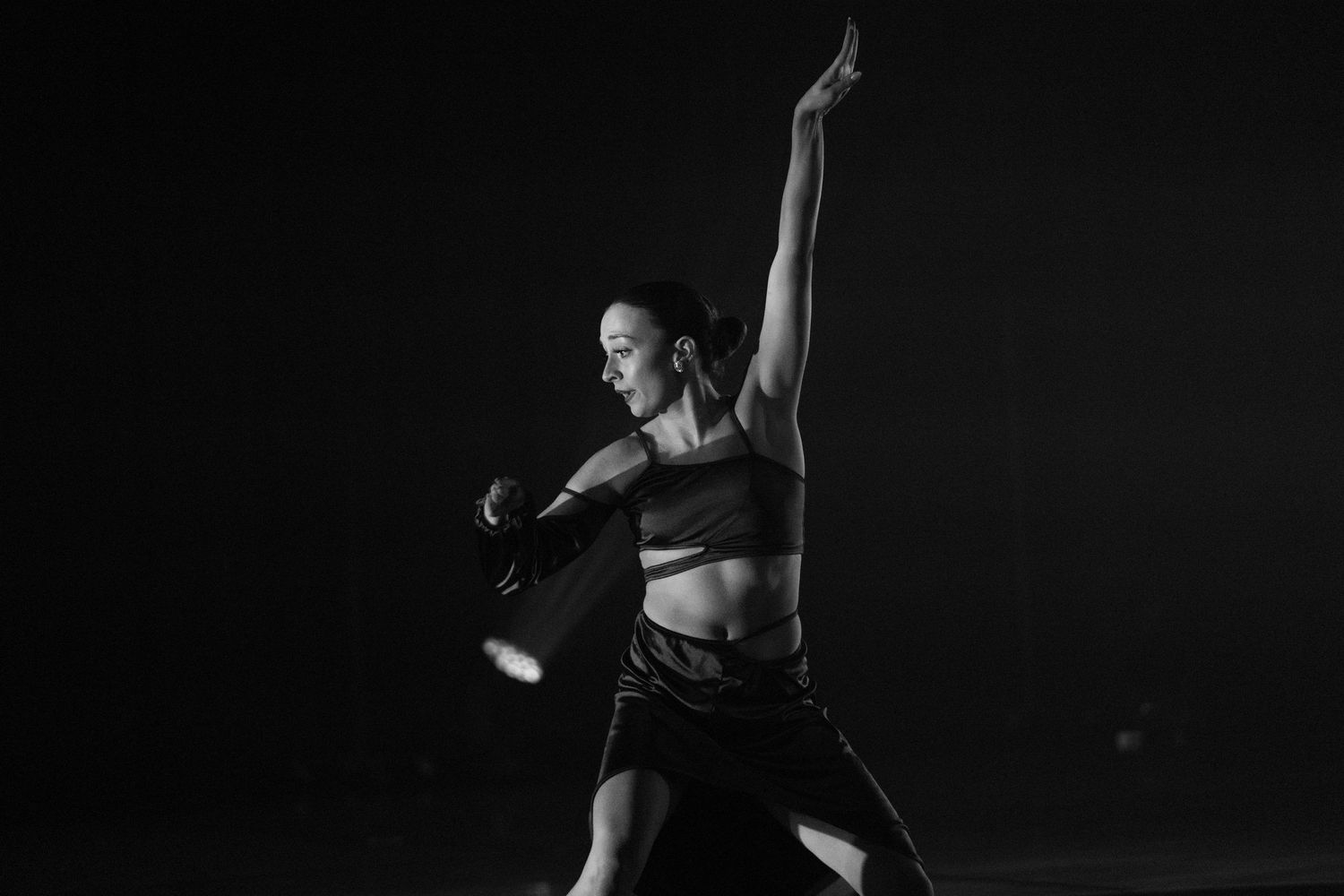 A dancer in athletic wear strikes a dramatic pose against a dark background during a contemporary dance performance.