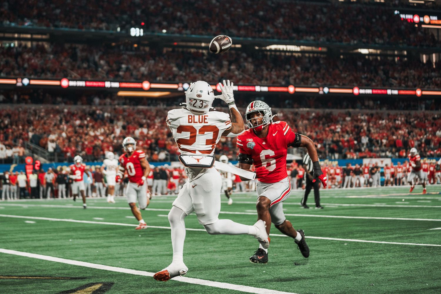 College football action shot with players competing for the ball in stadium setting.