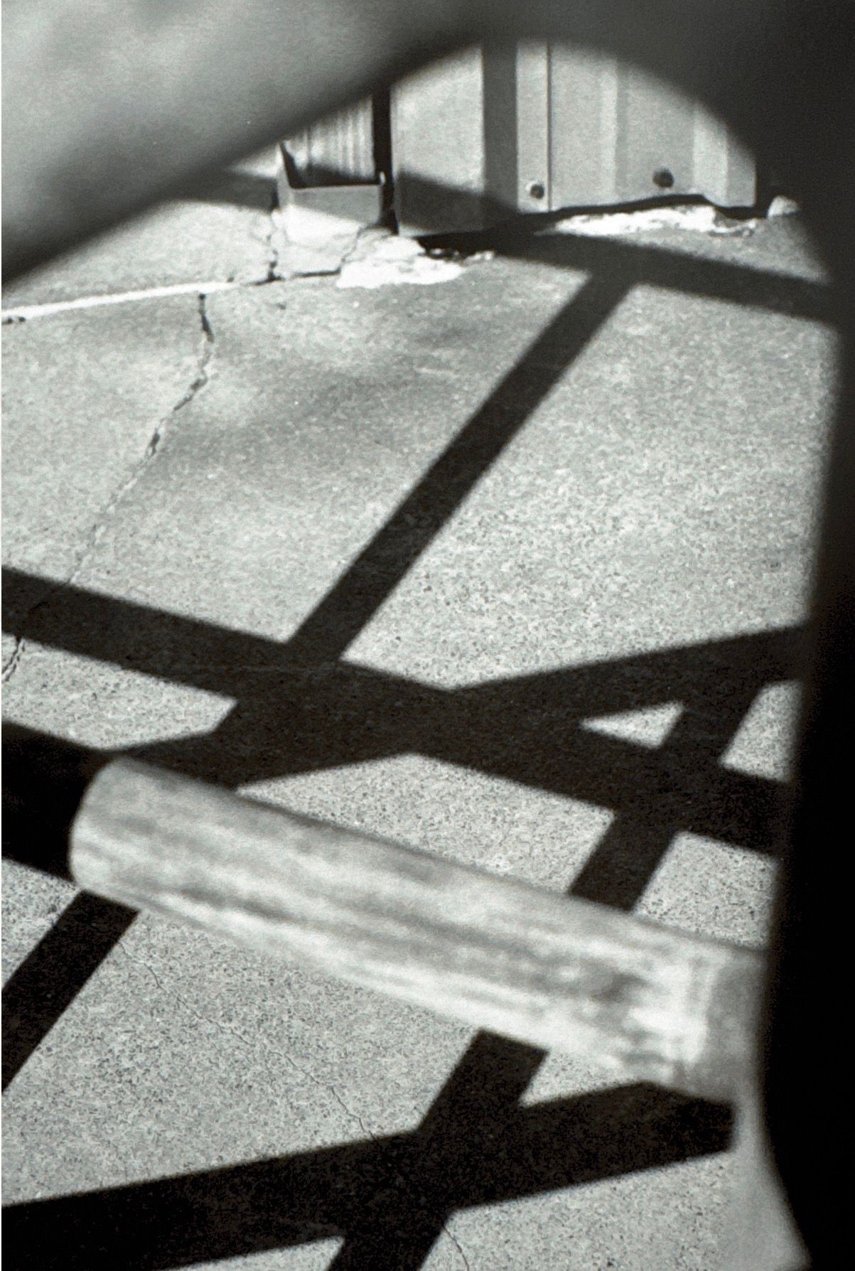Dramatic black and white shadows cast geometric patterns across a textured concrete surface in a minimalist composition.