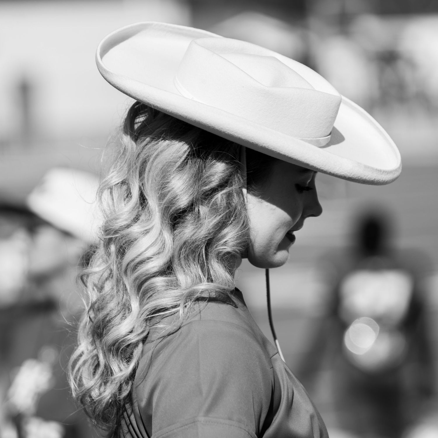 A black and white profile view of someone wearing a white cowboy hat with curled hair.