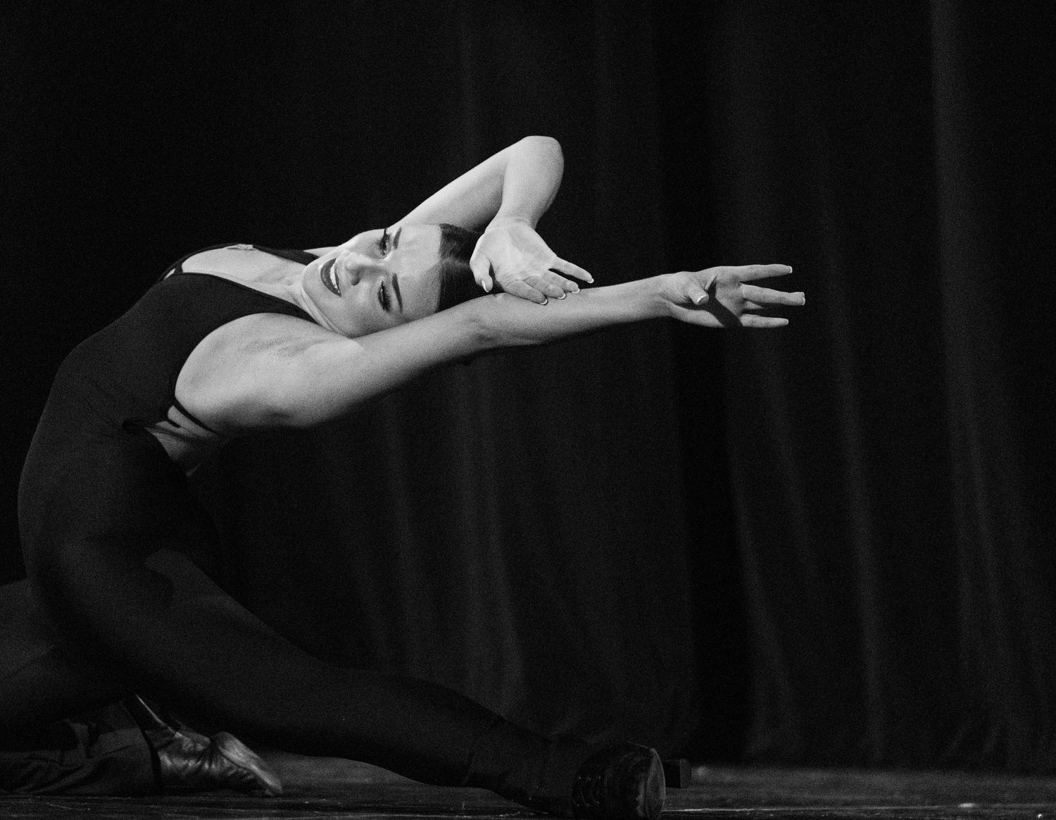 Black and white photo of a ballet dancer gracefully arching backward on stage in a dramatic contemporary dance pose.