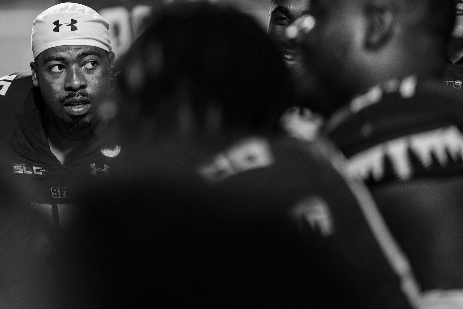 Athletes wearing Under Armour gear compete in an intense sporting event with dramatic lighting and dark background.