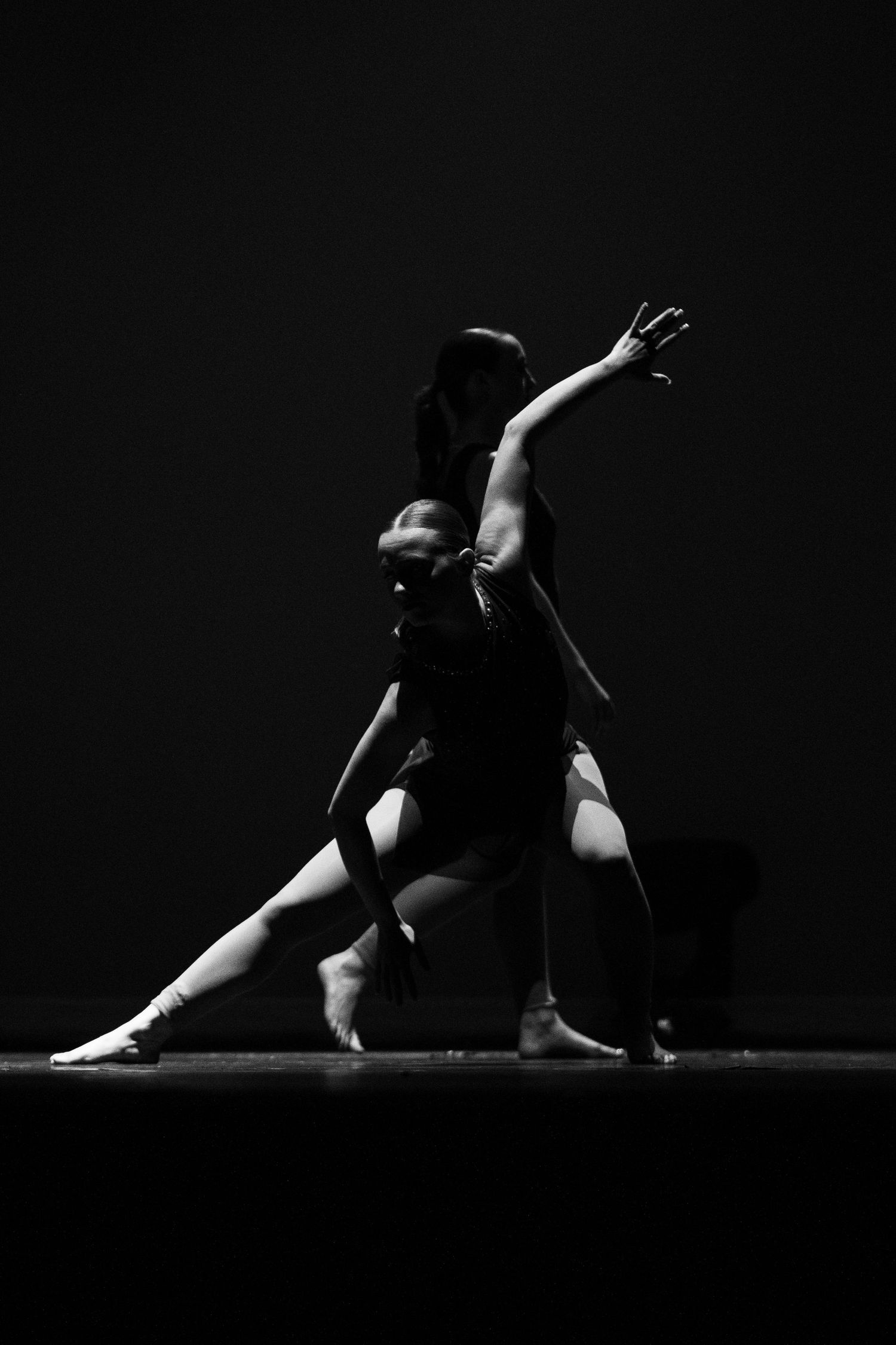 Two dancers perform a dramatic contemporary ballet duet in black and white, one arching back while the other extends upward.