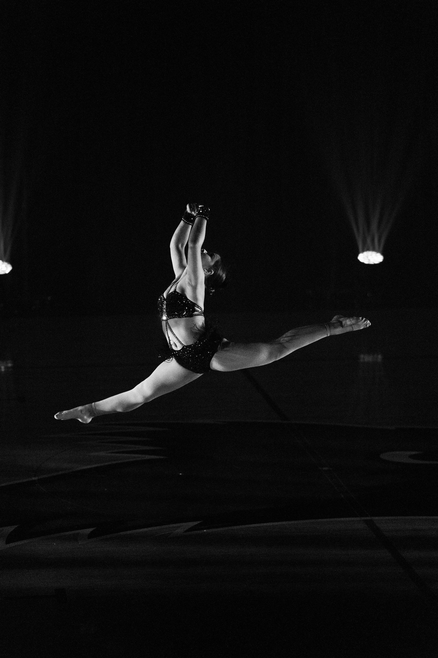 A dancer executes a powerful split jump in mid-air during a dramatic stage performance.