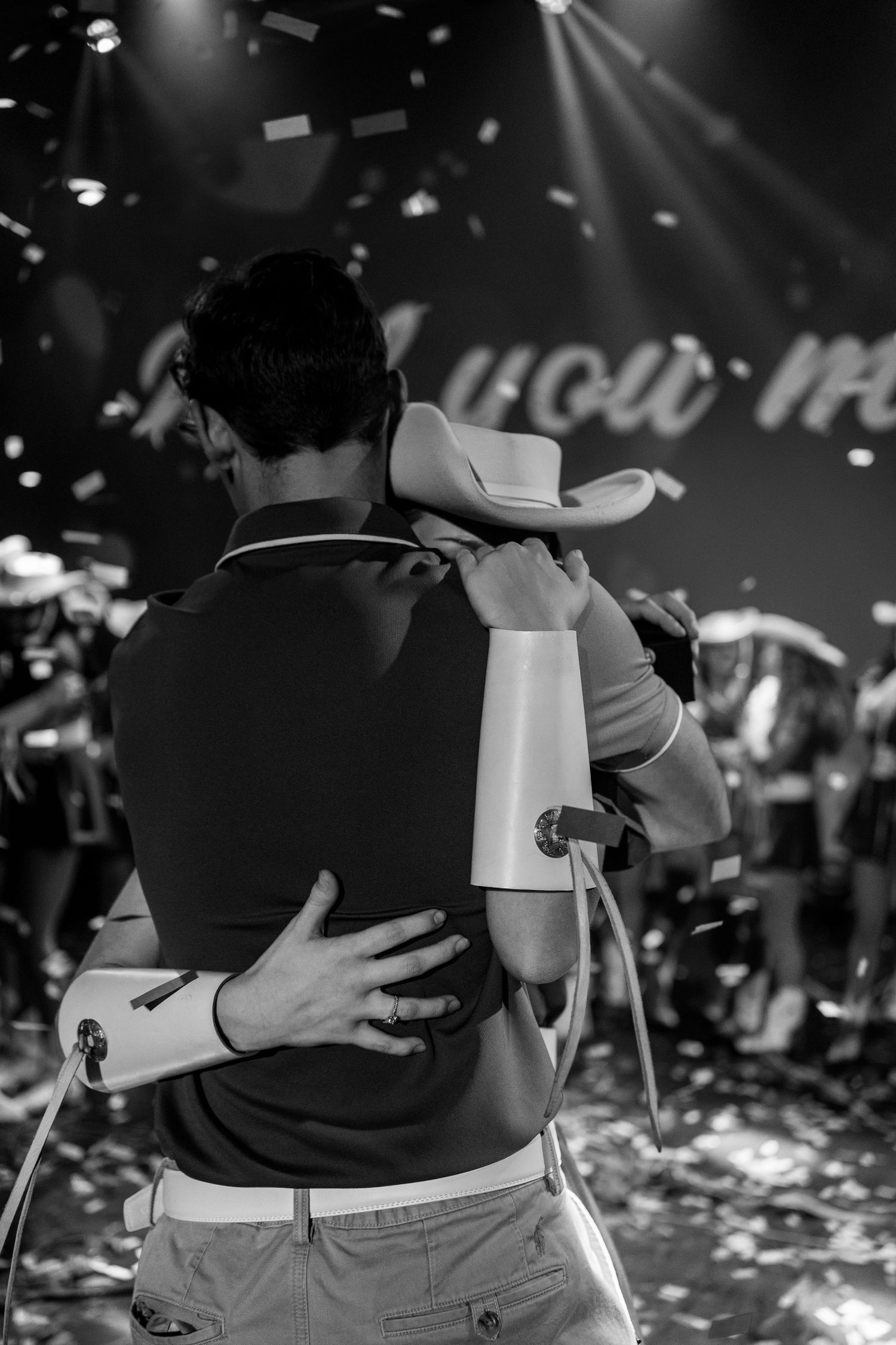Black and white image of two people embracing during a confetti-filled celebration.