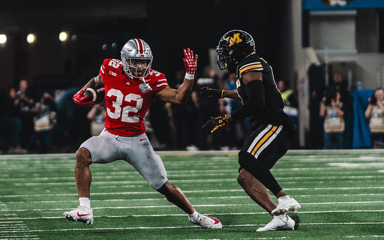 Ohio State football player #32 in red uniform defends against a Missouri player in black during a night game.