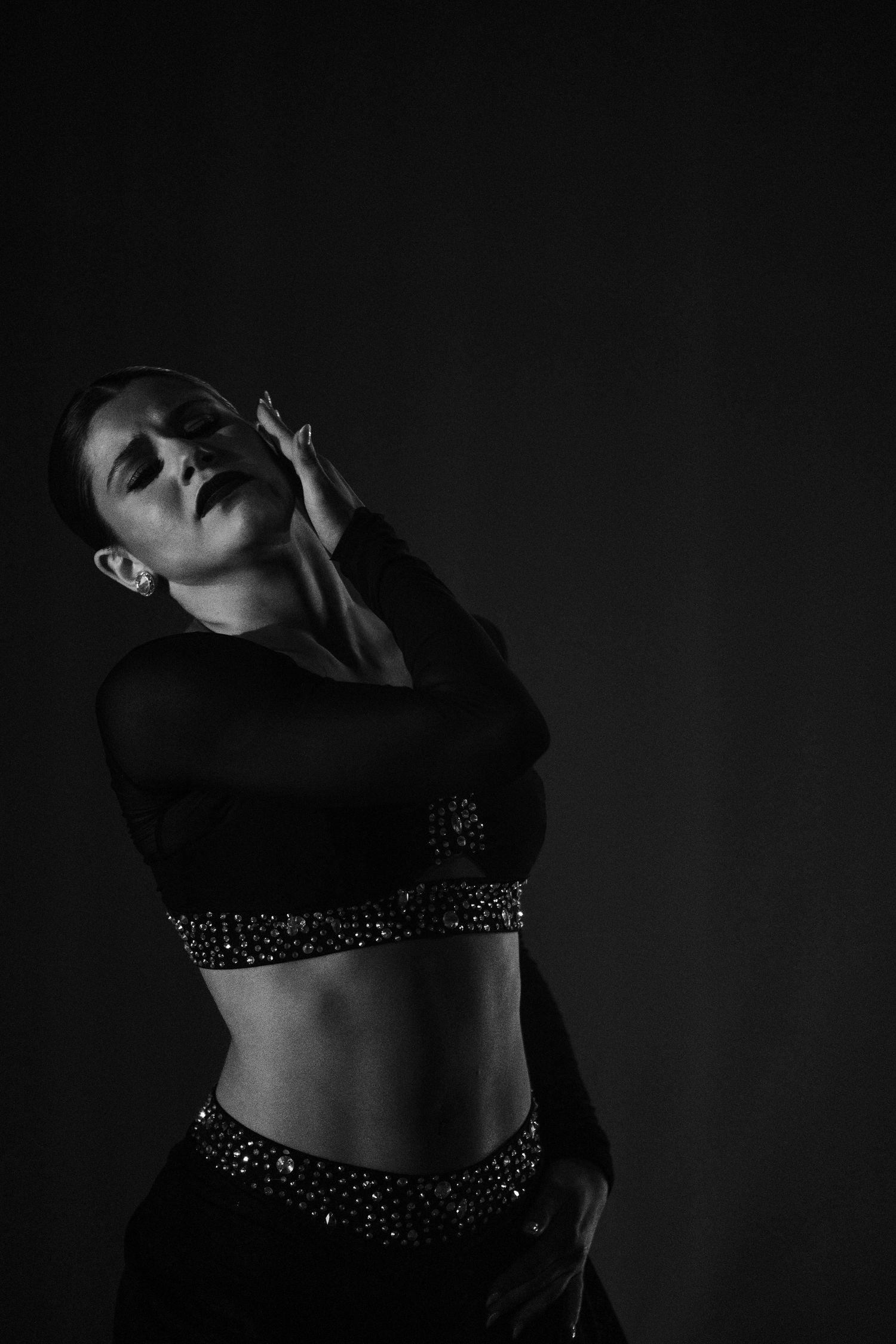 Black and white photo of a woman in a sparkly crop top and skirt, posing dramatically against a dark background.