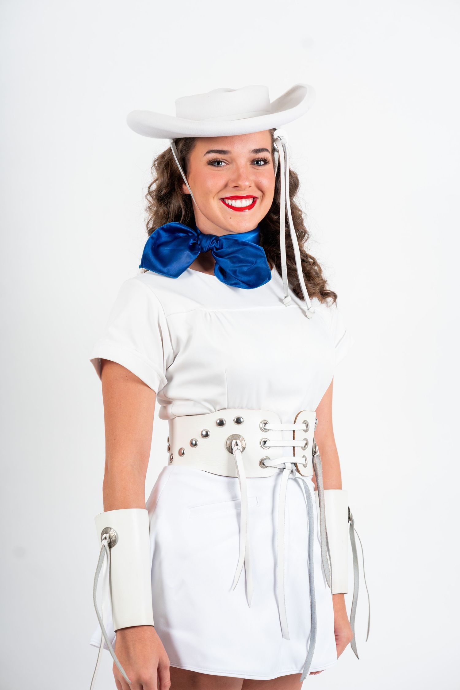 A fashion model wearing a white top with blue scarf accessory poses against a light background.