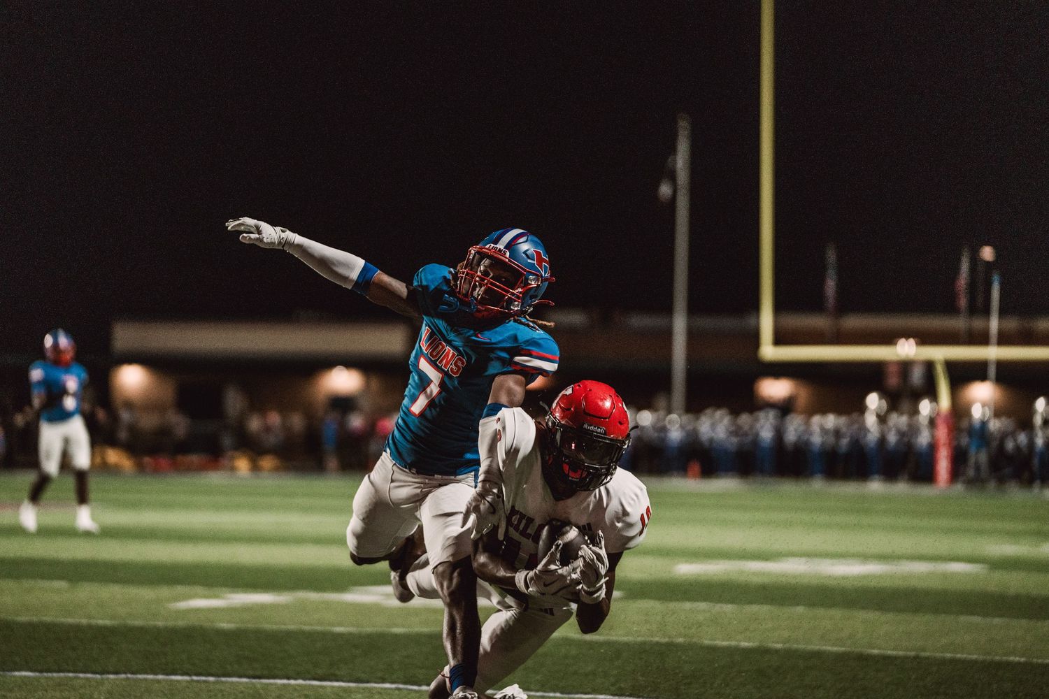 Football player in blue and white uniform dives to make a catch during a nighttime game on artificial turf.