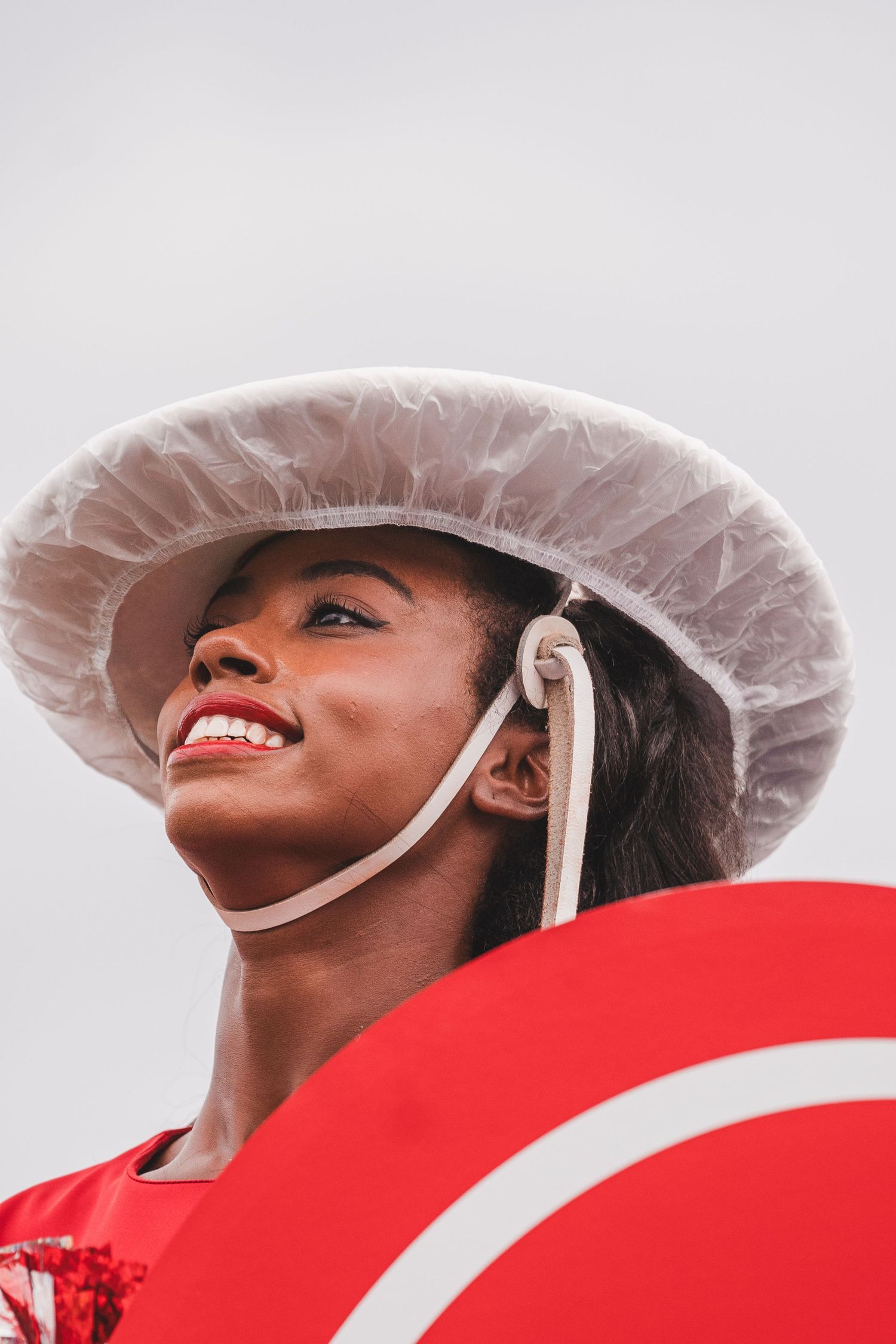 Person in white disposable hair cover smiling against red and white background while looking upward.