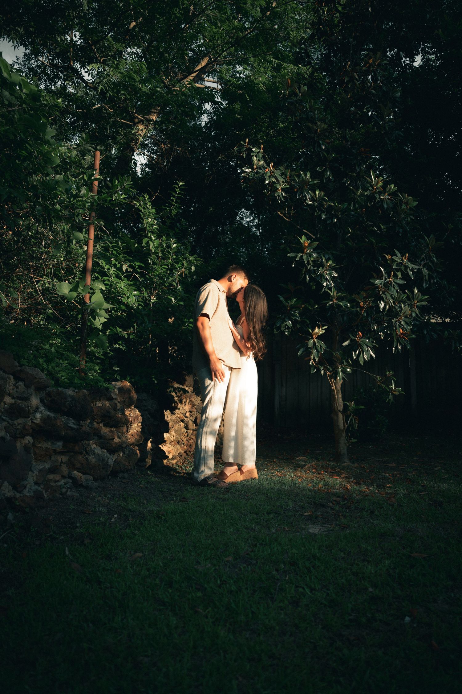 A couple embraces in a romantic golden hour moment amid a shadowy wooded landscape for their wedding photos.