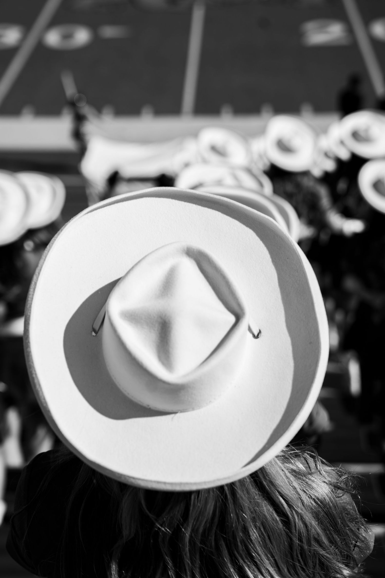 Black and white image showing a row of people wearing white cowboy hats at an event.