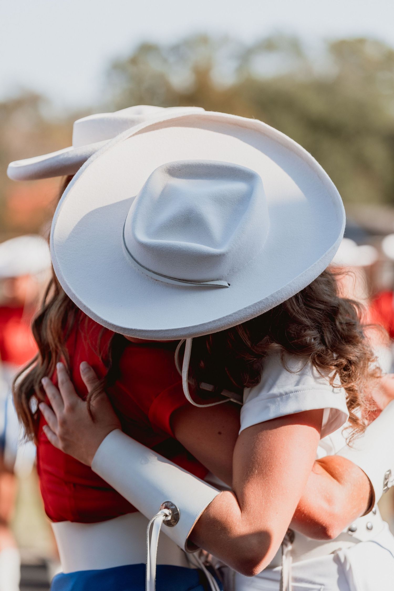 Two people share an intimate kiss while wearing white cowboy hats at an outdoor event.