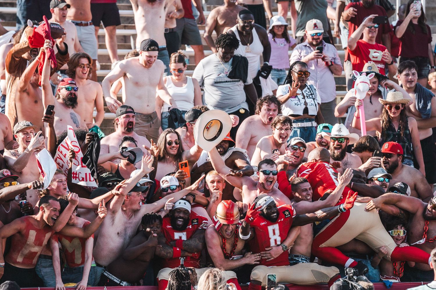 Excited sports fans in red and white colors celebrate enthusiastically in crowded stadium stands during a game.