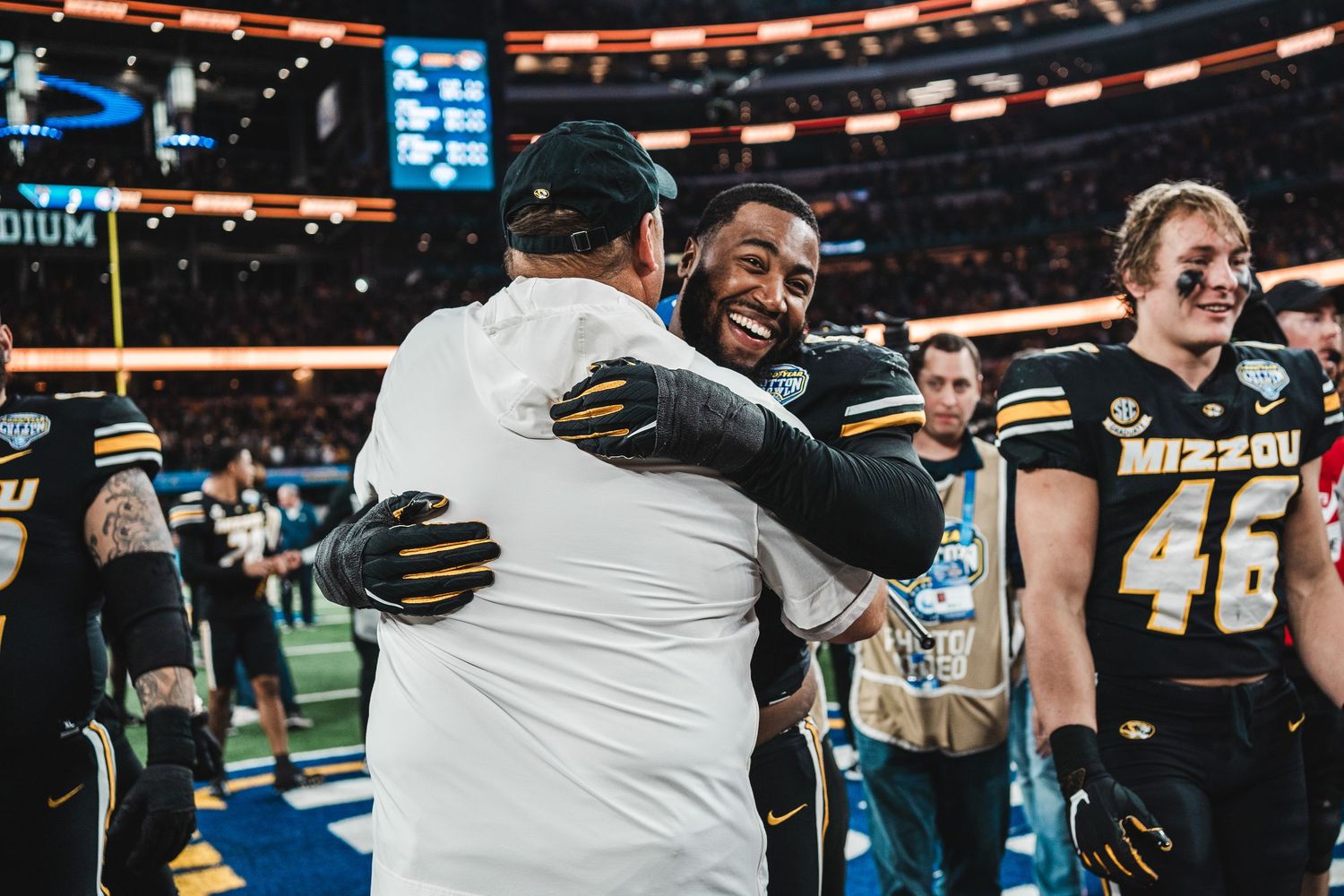 University of Missouri football players and coaches embrace in celebration on the field after a game.