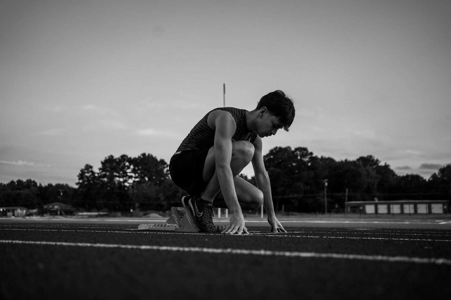 Black and white photo of an athlete in starting position on a running track.