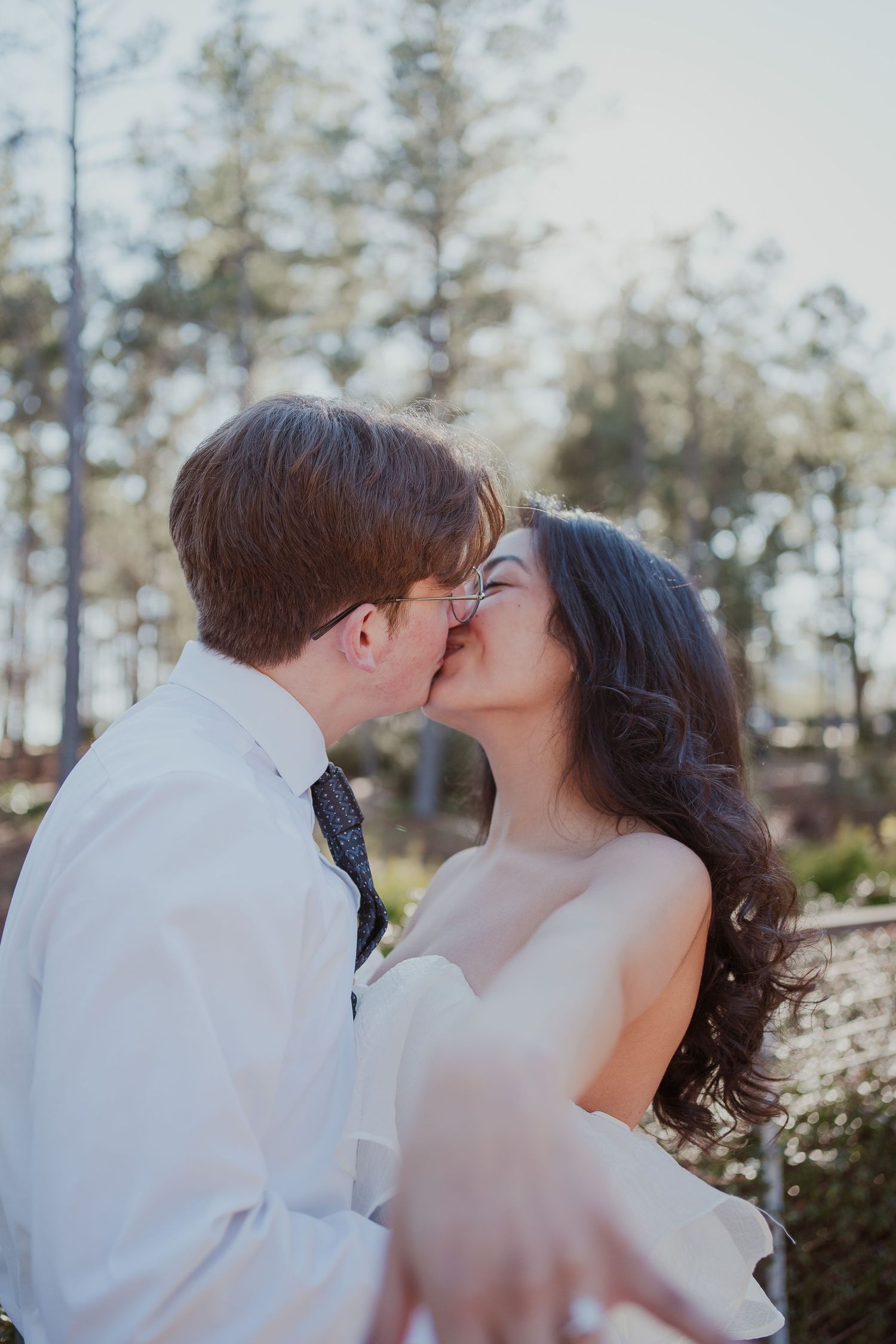 Romantic wedding couple sharing a kiss outdoors with pine trees in background.