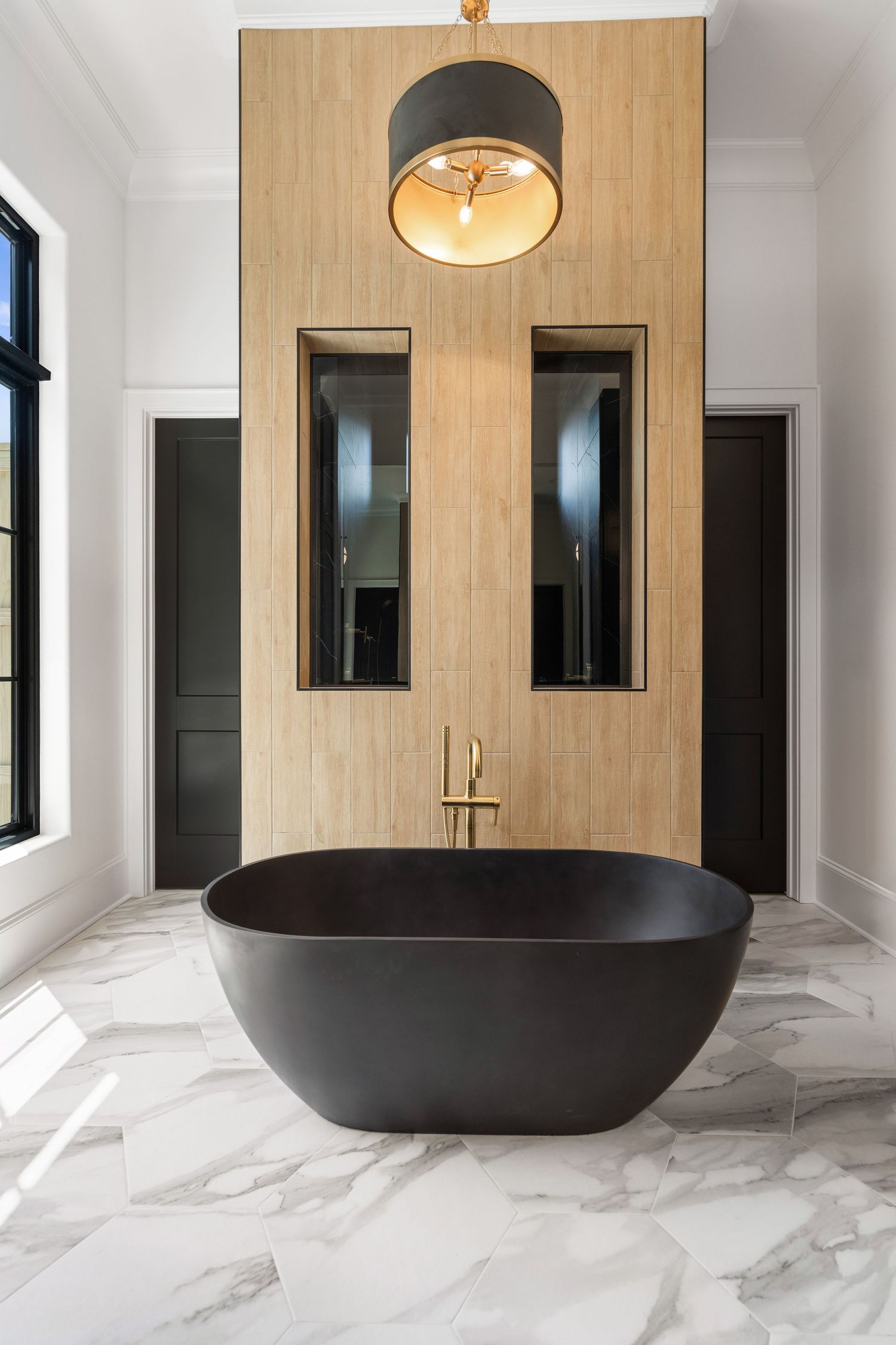 Modern bathroom with black freestanding tub, wooden accent wall, and contemporary ceiling light fixture.