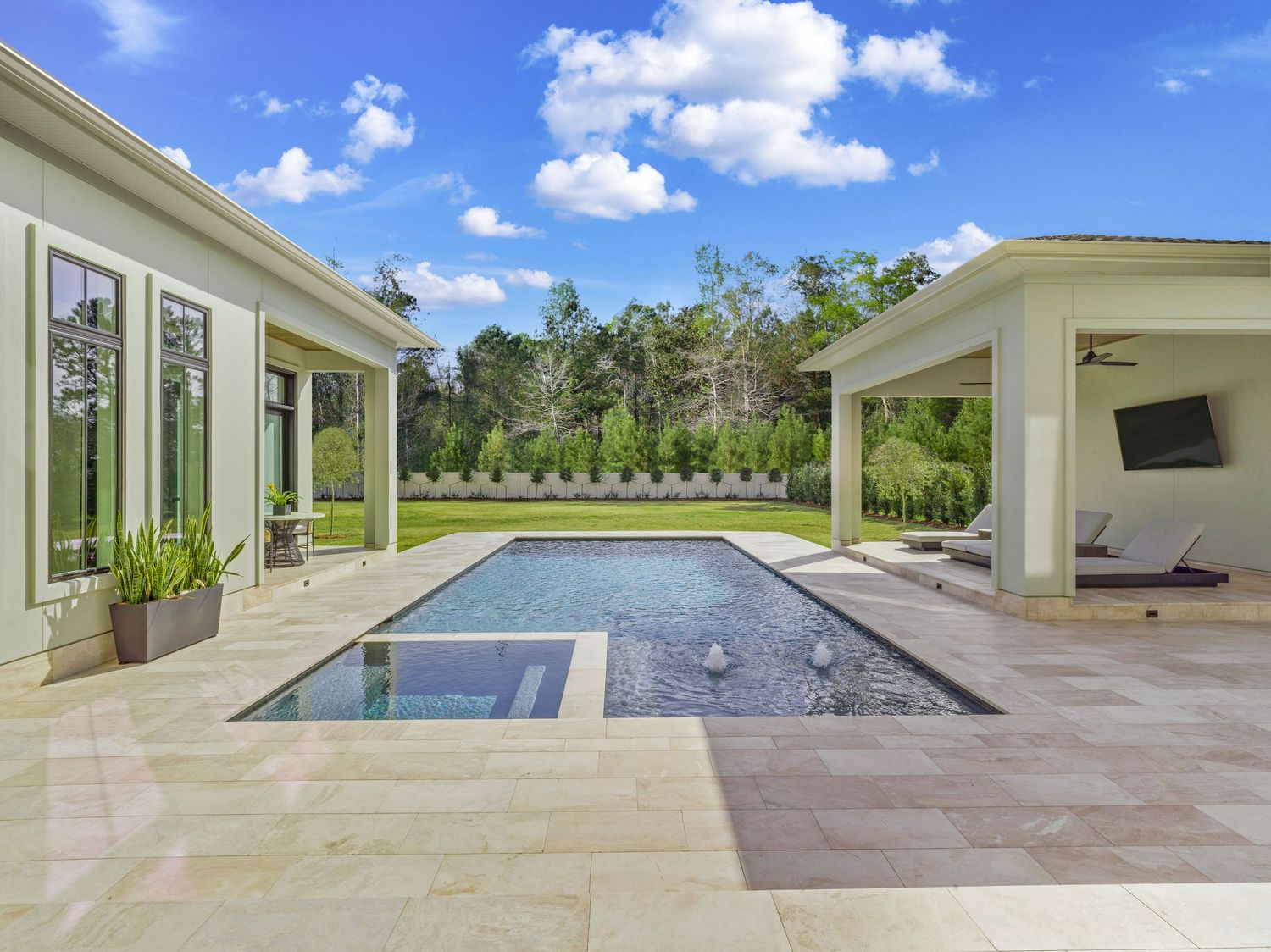 Luxury backyard featuring a rectangular pool with spa, surrounded by covered patios and stone decking.