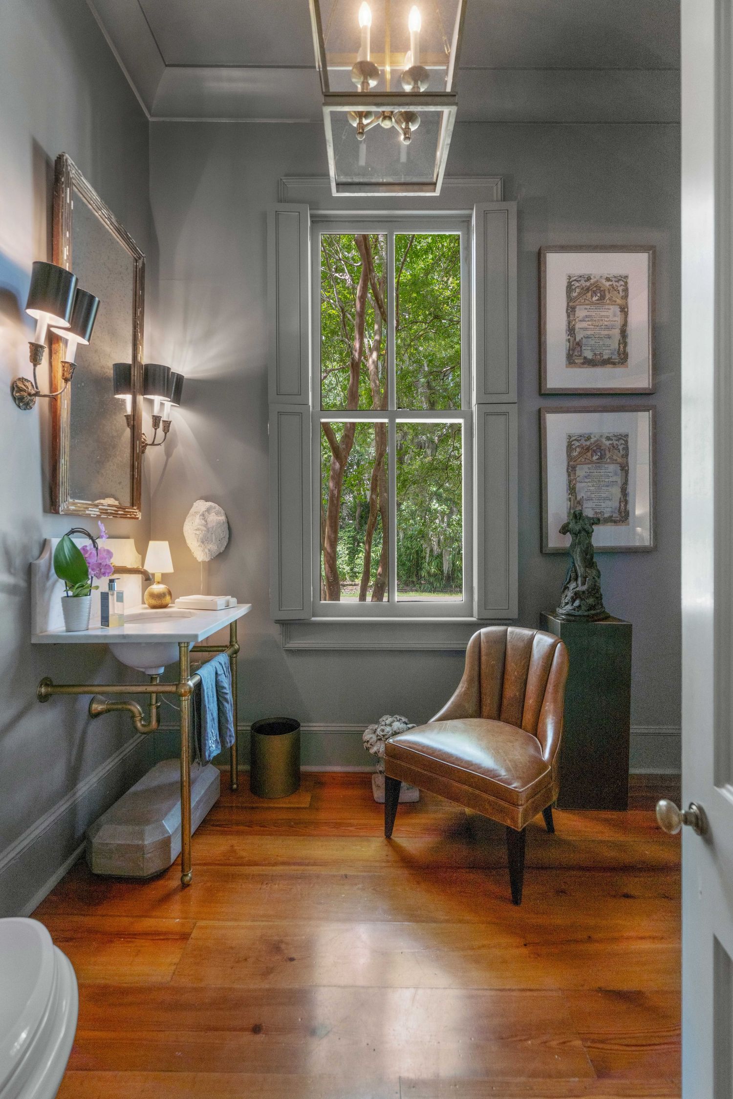 Cozy corner with gray walls, hardwood floors, and a leather chair beside a tall window with natural light.