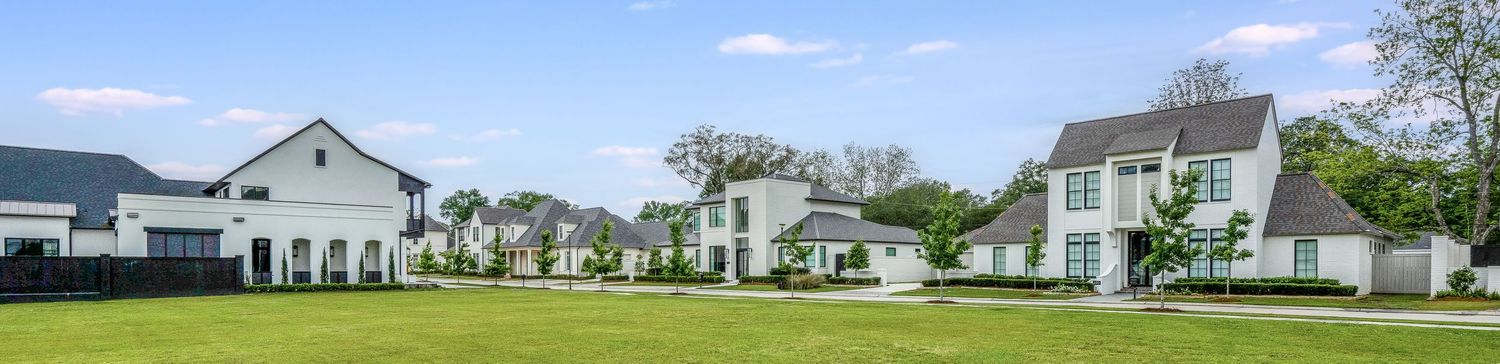Panoramic view of luxurious white modern homes with manicured lawns under blue sky.