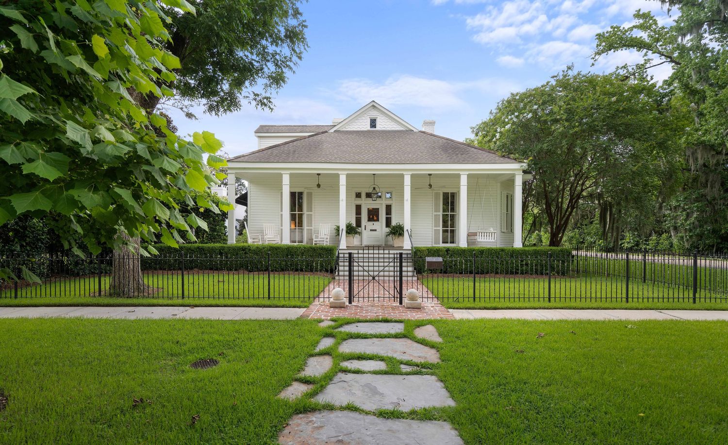 Traditional Southern-style white house with wraparound porch and stone pathway through manicured front lawn.