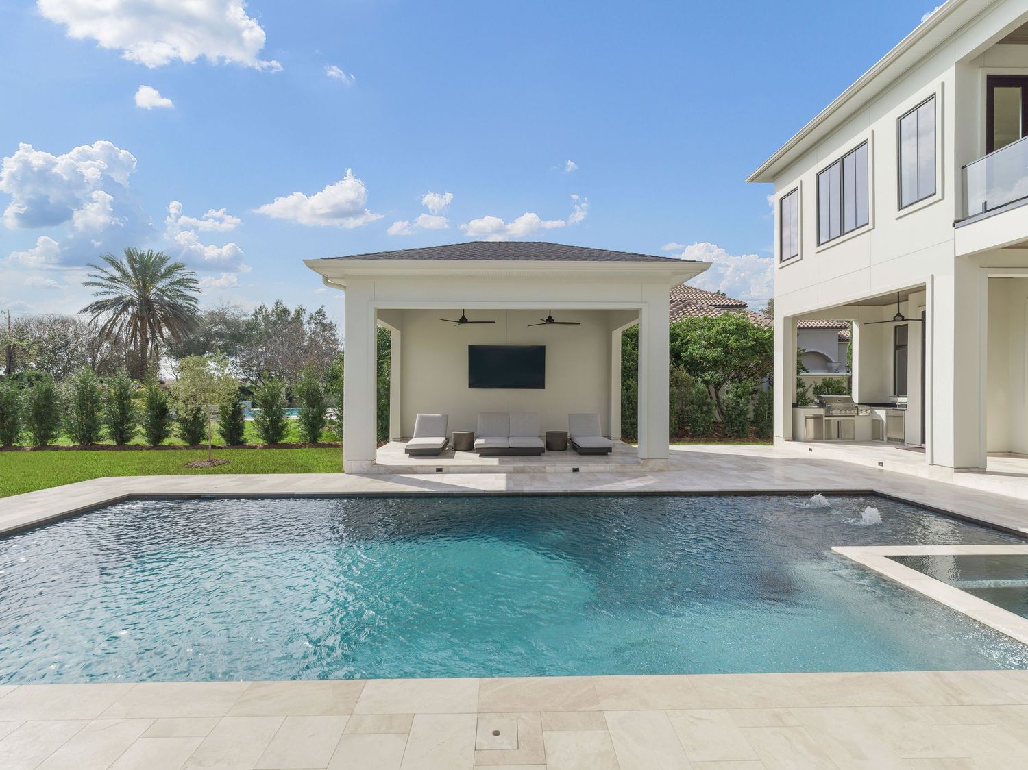 Modern poolside outdoor living space with covered pavilion and entertainment area overlooking a geometric swimming pool.