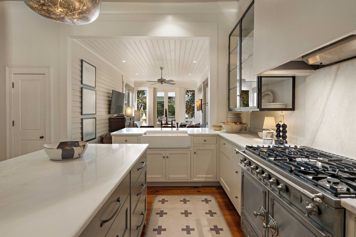 Modern white kitchen with quartz countertops, gas range, and patterned tile floor runner.