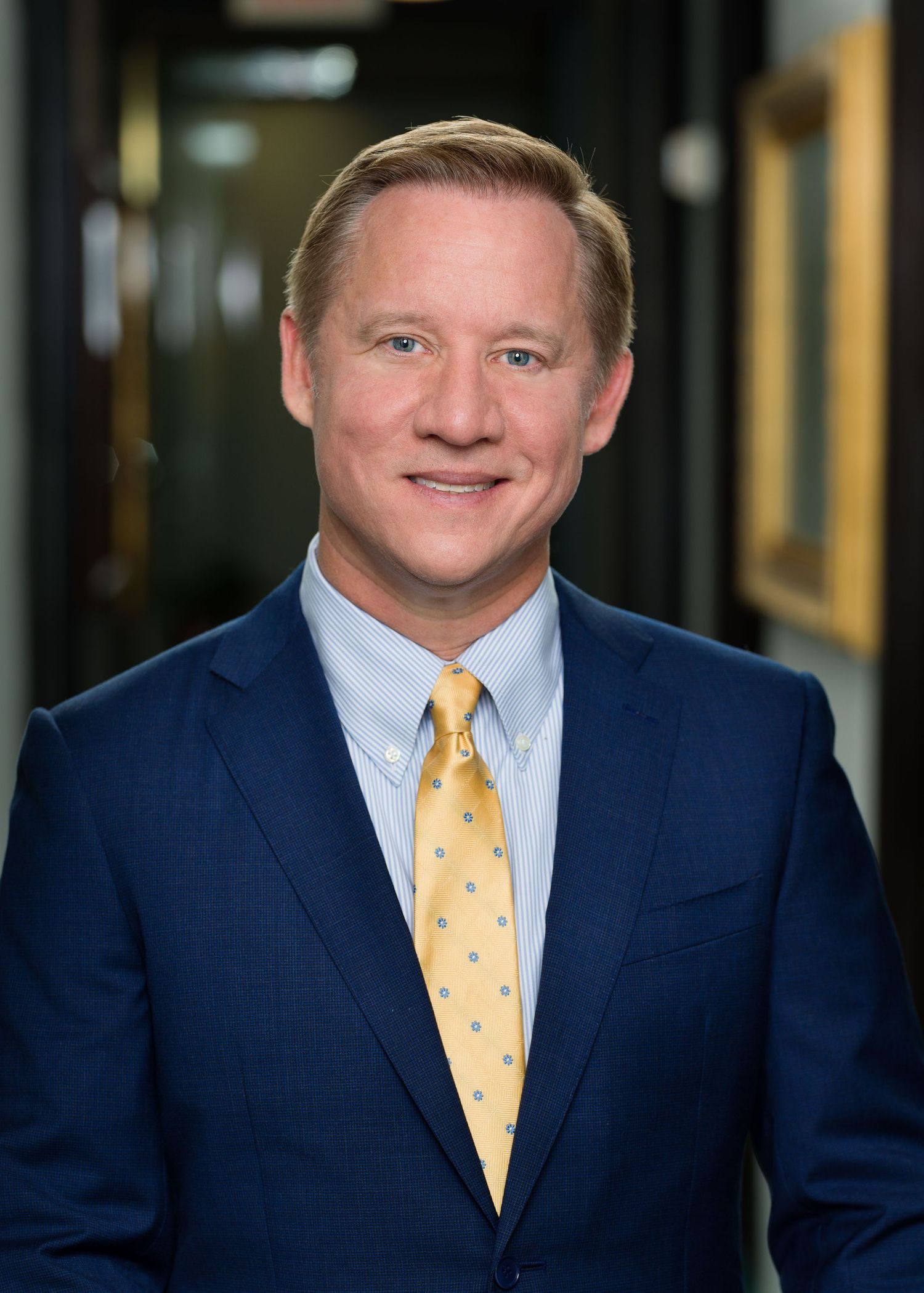 Professional business portrait of executive wearing navy suit and yellow polka dot tie.
