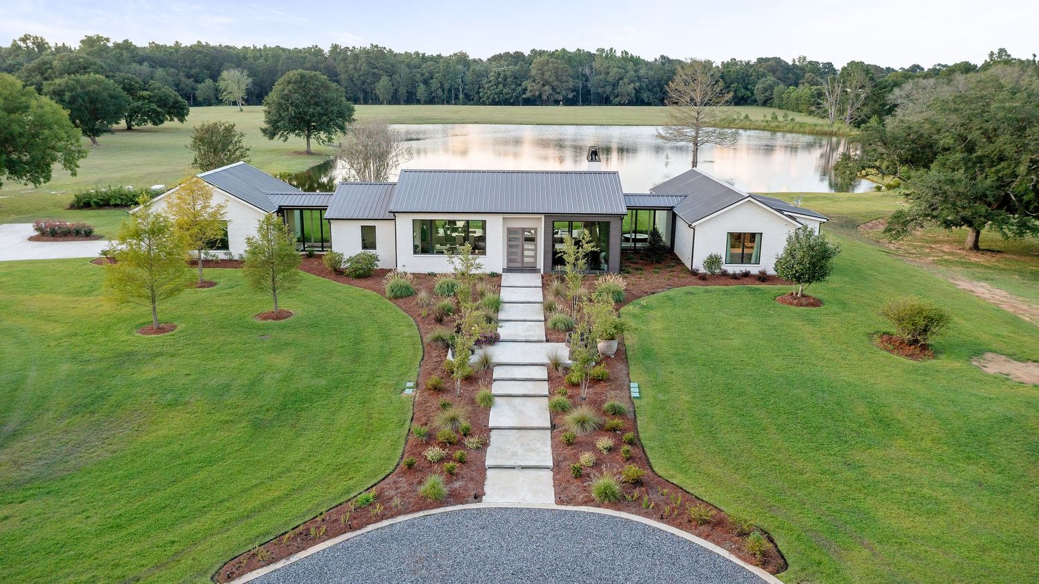 A panoramic view of a residential property with green lawns, landscaping and a white house surrounded by trees.