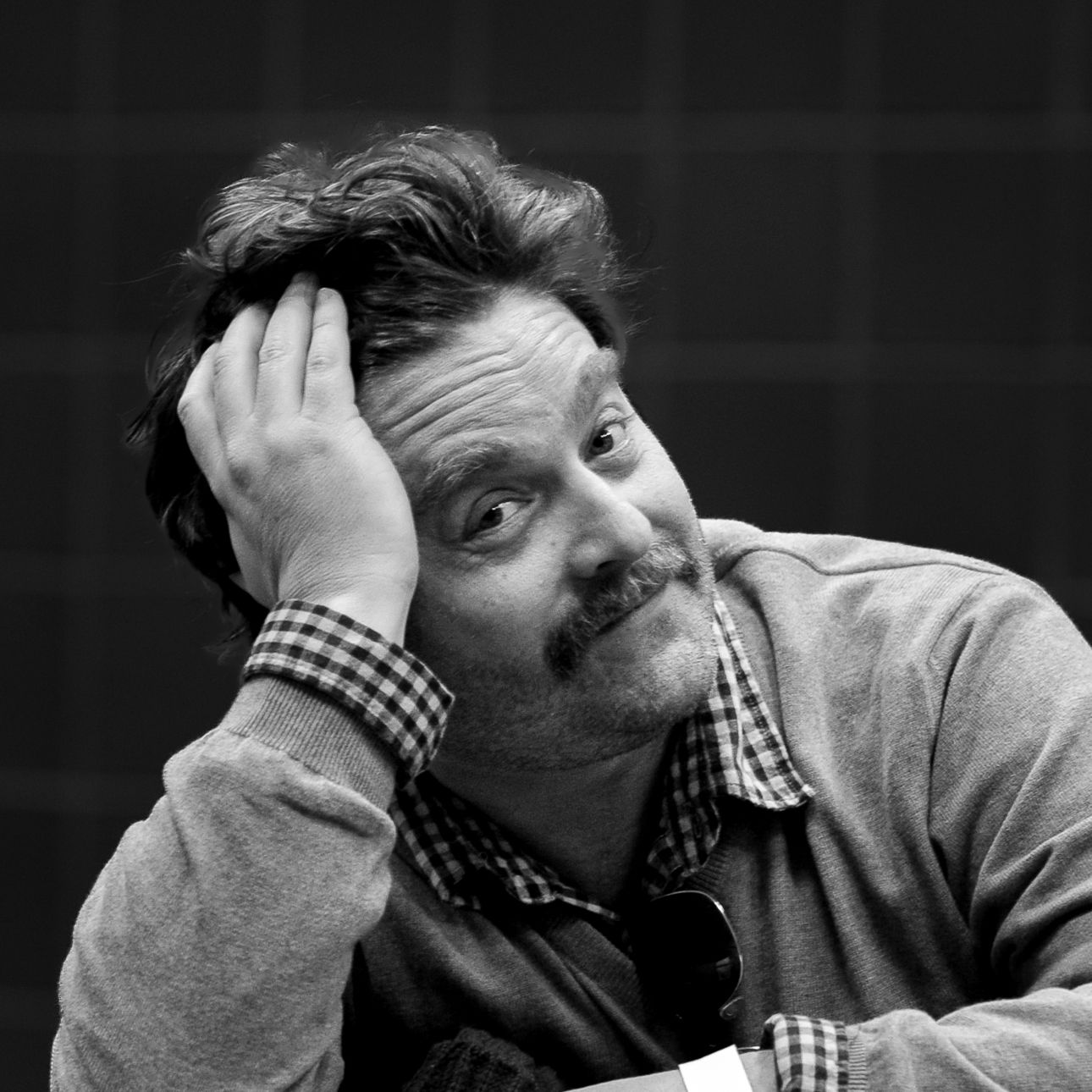 Black and white portrait of performer in checkered shirt resting head on hand with contemplative expression.
