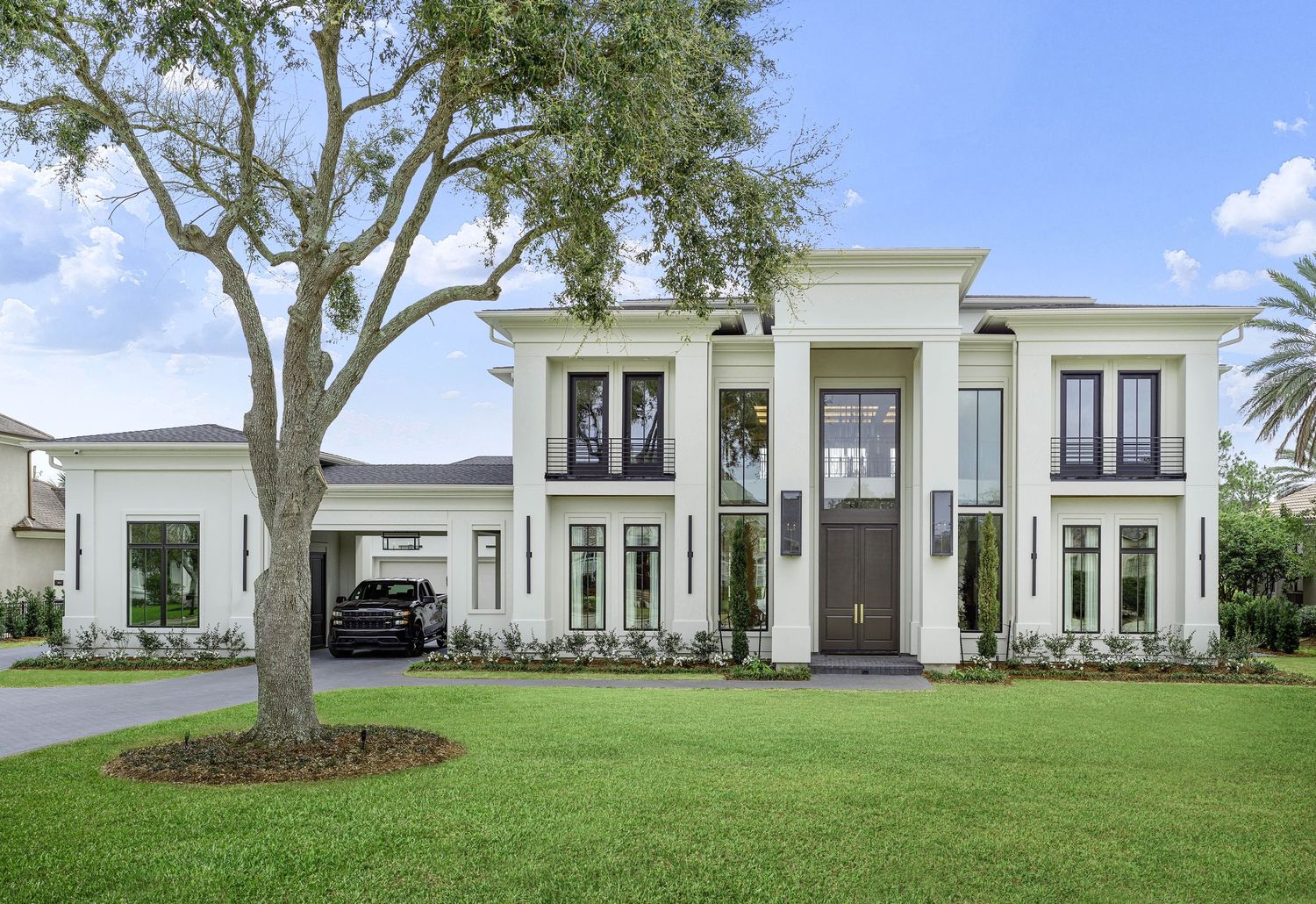 Elegant white luxury home exterior with mature oak trees and manicured landscaping.