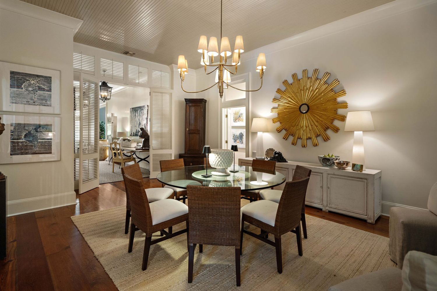 Formal dining area featuring round table, leather chairs, and gold sunburst mirror in white painted room.