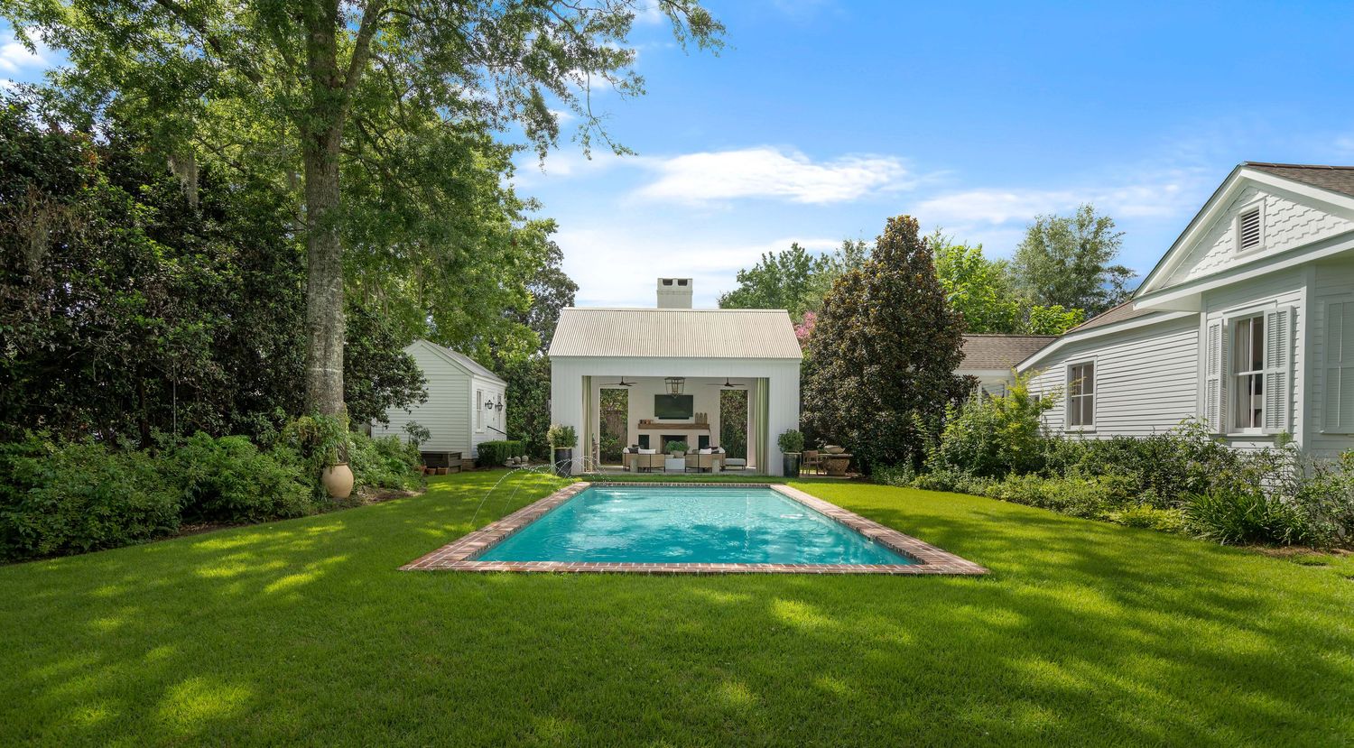 Elegant white house with pool featuring symmetrical design and beautiful landscaping in the backyard.