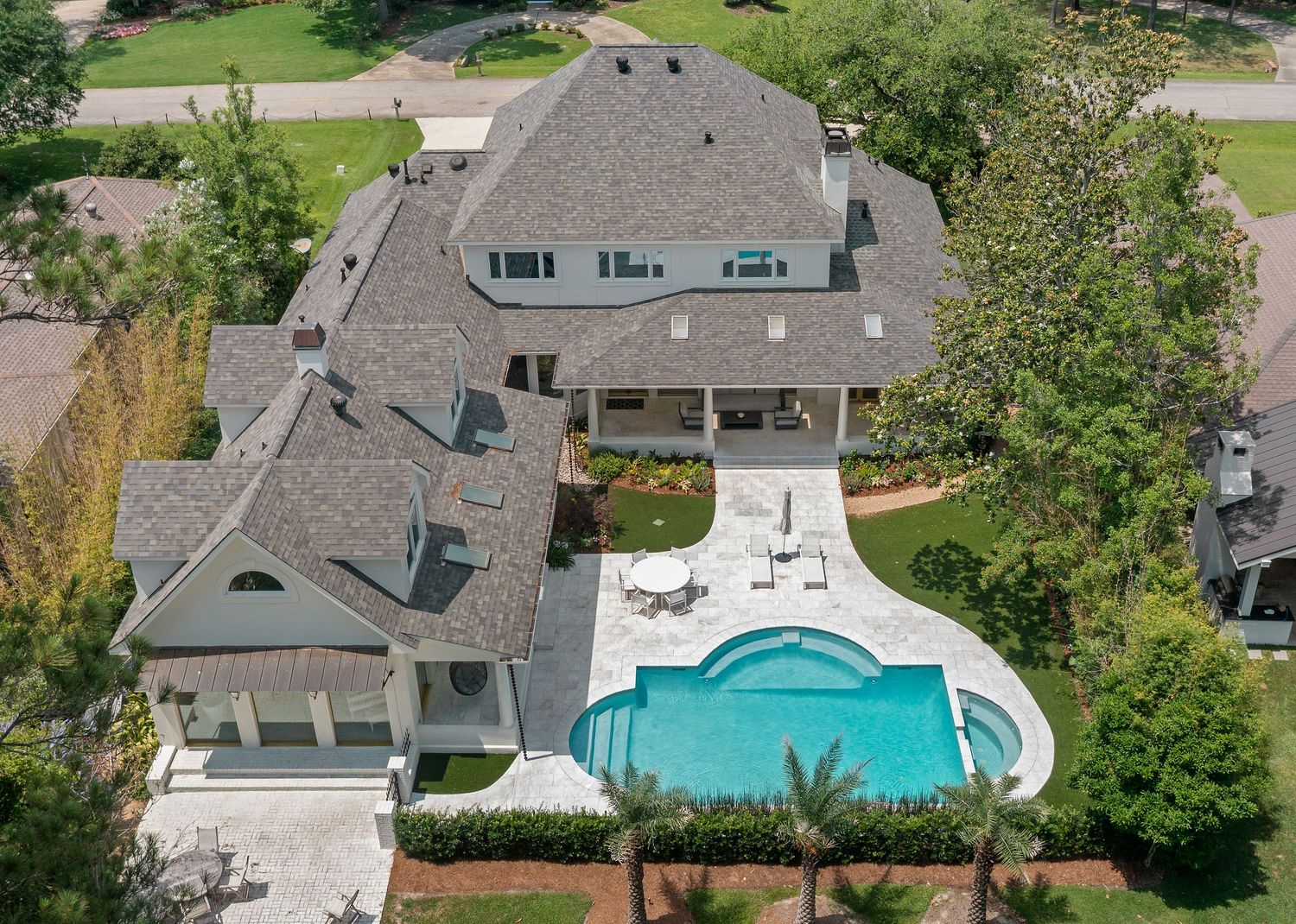 Aerial view of luxury home with gray shingled roof and curved swimming pool in landscaped backyard.