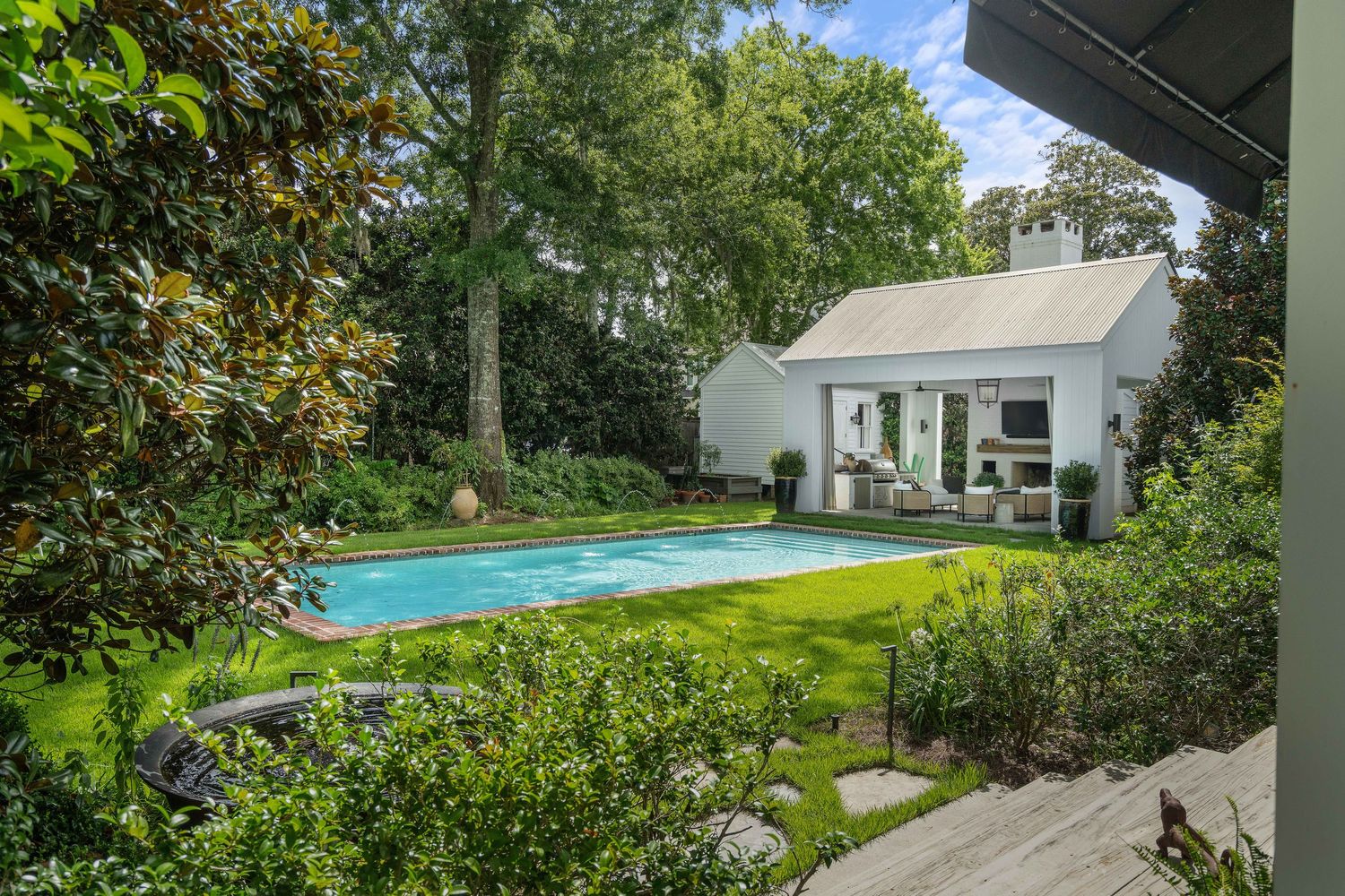 Luxurious backyard featuring a rectangular swimming pool and small white poolhouse surrounded by lush landscaping.