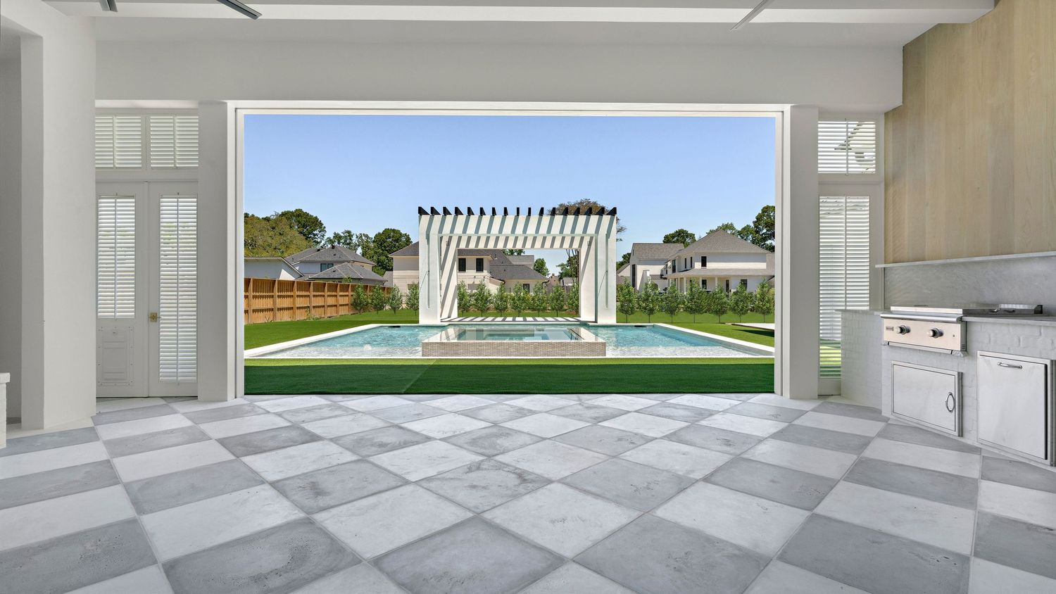 Spacious indoor-outdoor living space with checkerboard flooring opens to a backyard with pergola and manicured lawn.