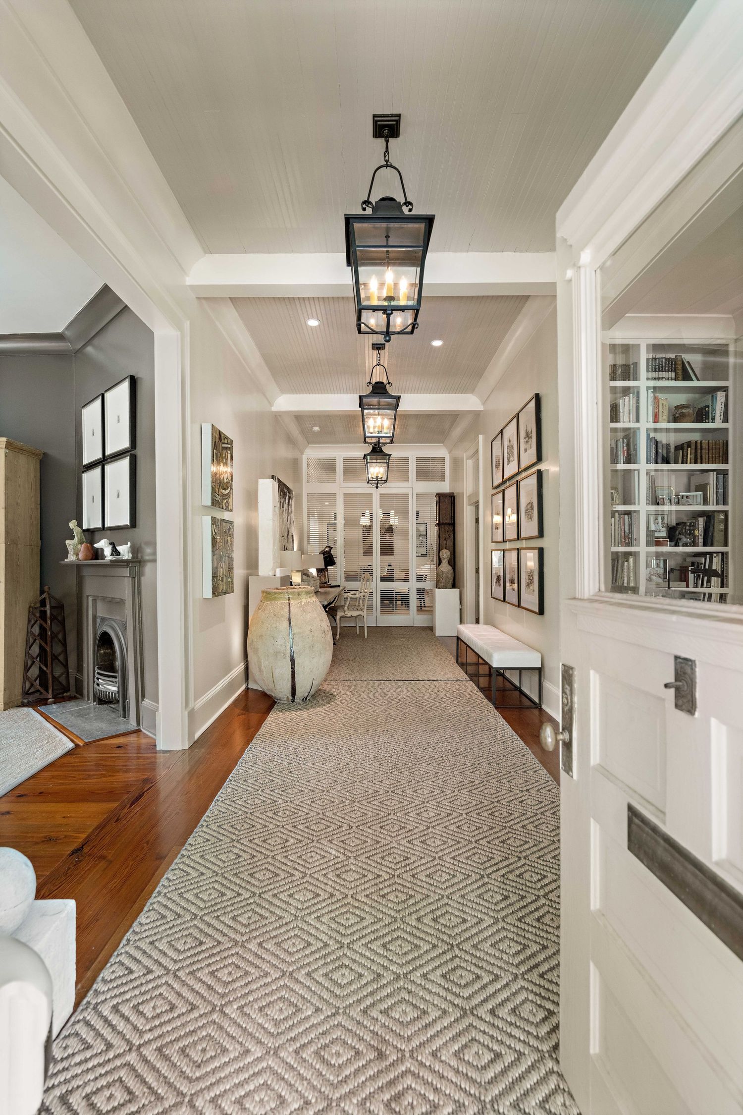 Elegant hallway with hardwood floors, lantern pendant lights, and a geometric patterned rug leading to built-in shelving.