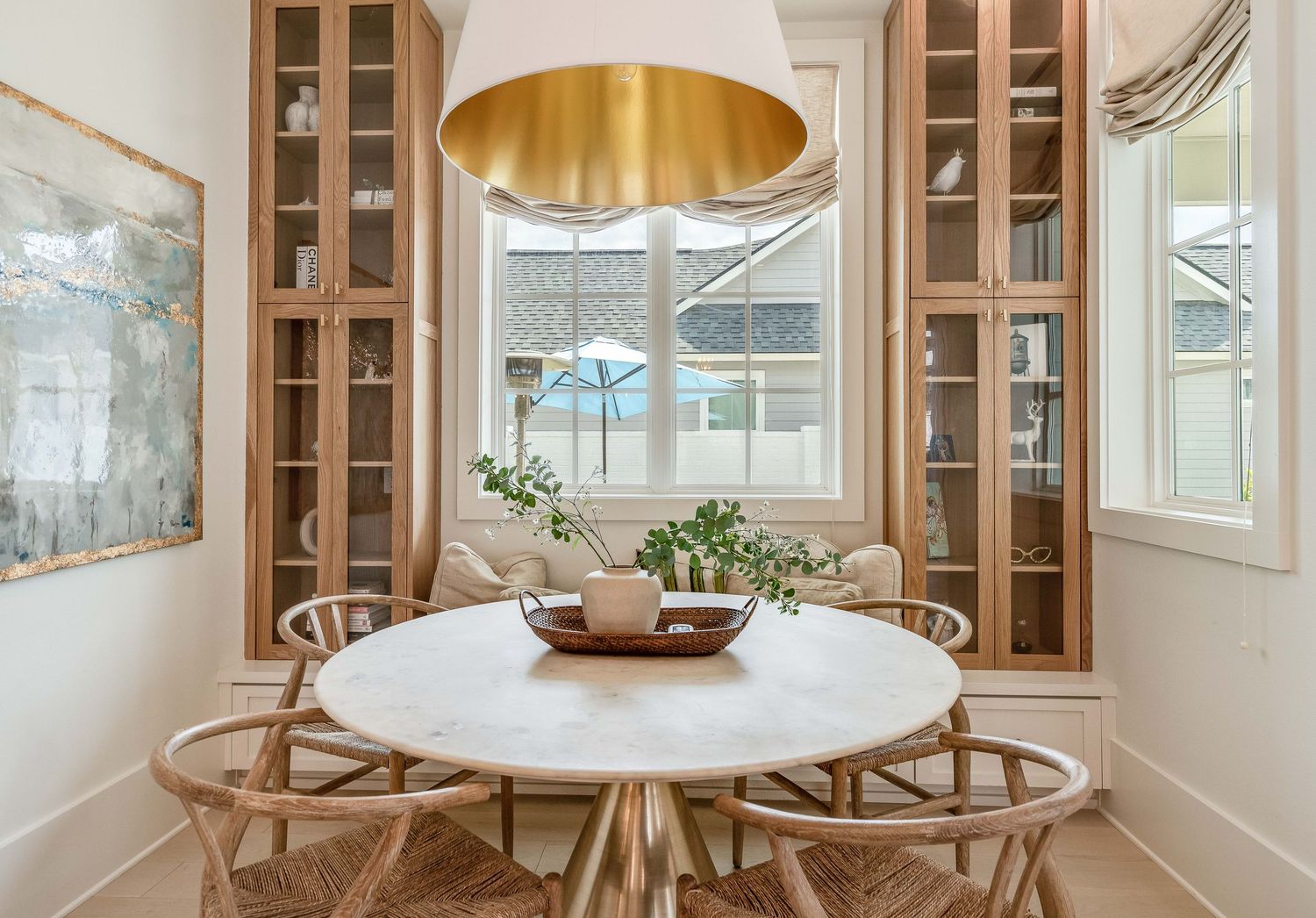 Modern dining room featuring wooden chairs and round table under gold pendant lighting.
