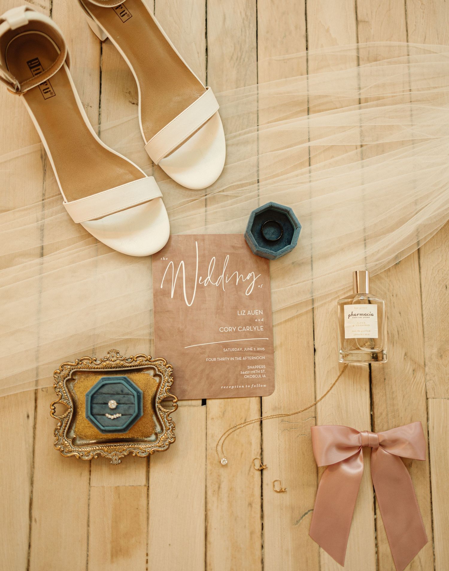 Wedding accessories and invitations laid out on a light wooden floor including shoes, bows, and paper items.