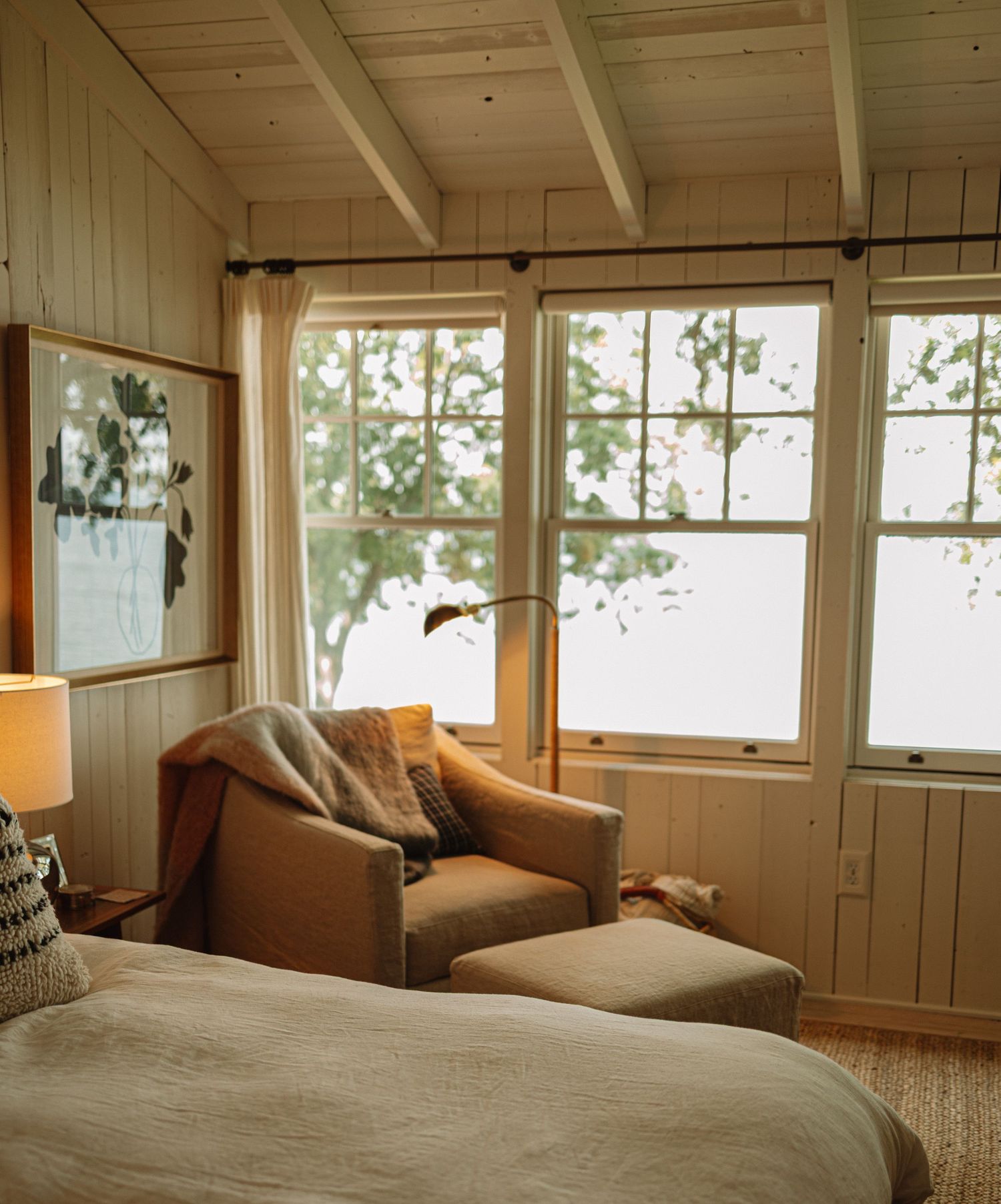 A panoramic view of a cozy bedroom with wooden walls and windows overlooking pine trees in natural sunlight.