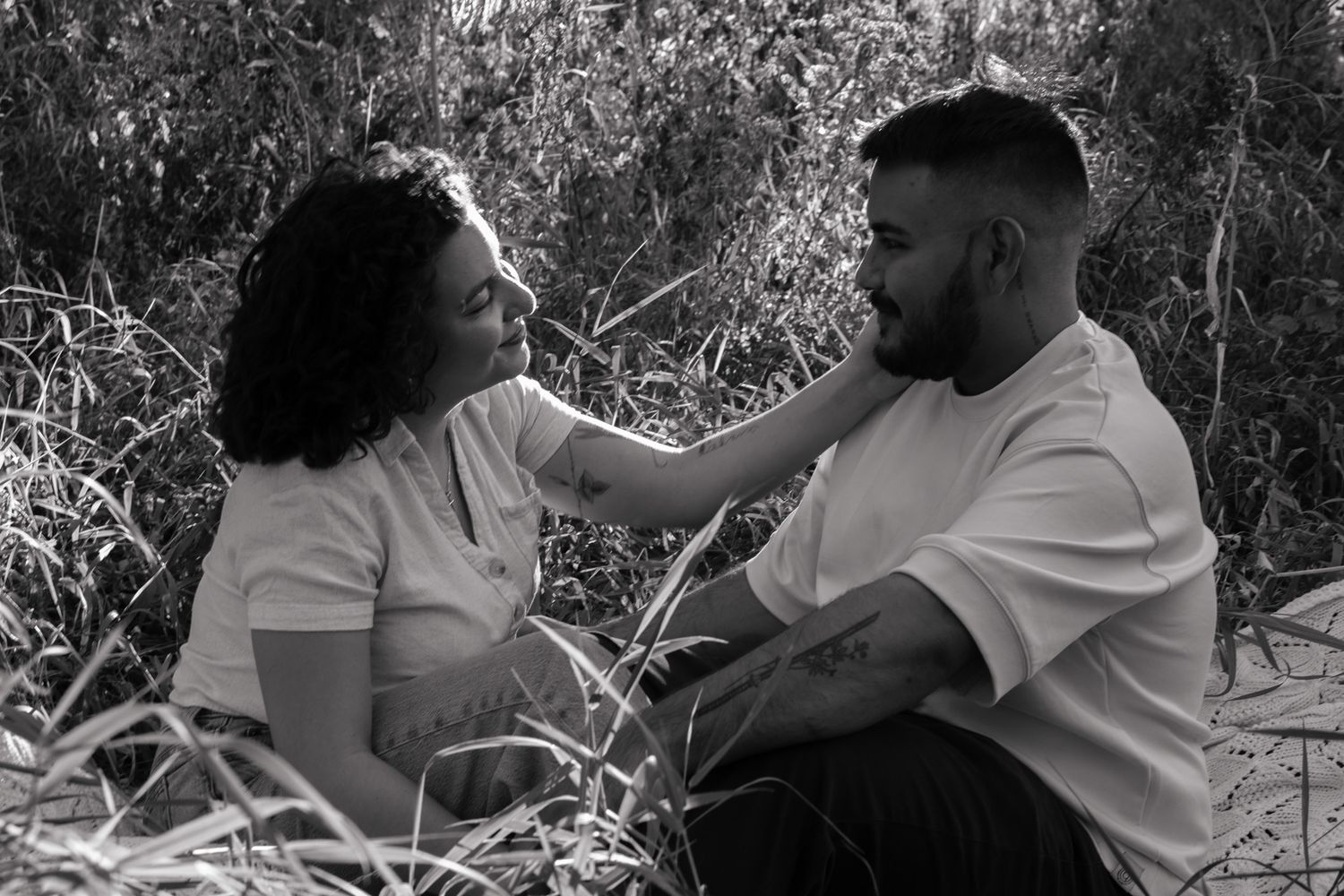 Couple sitting together in tall grass having an intimate conversation in black and white.