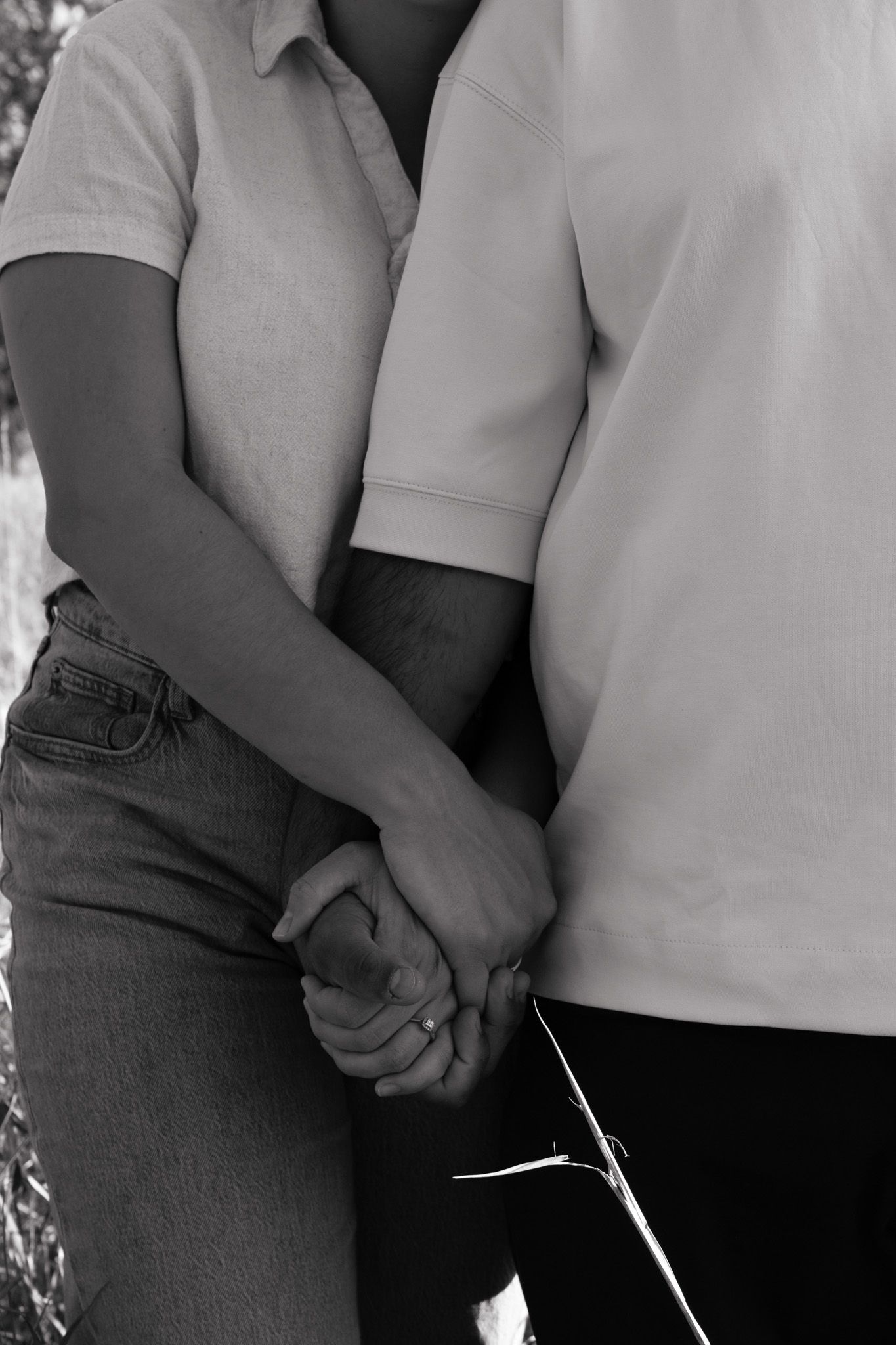 Close-up black and white image of two people holding hands while wearing casual clothing.
