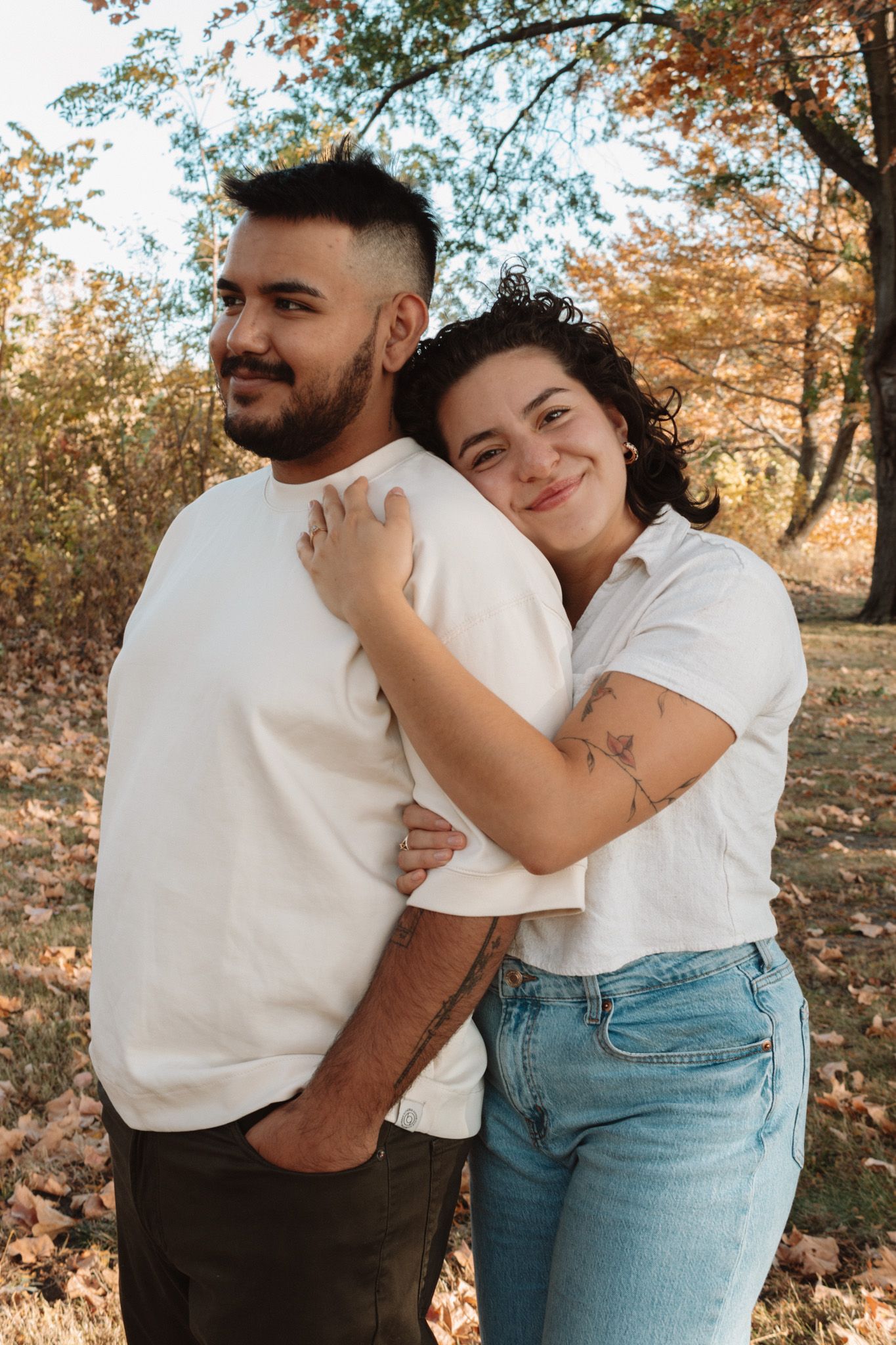 Couple embraces warmly in an autumn park setting with golden sunlight filtering through trees.